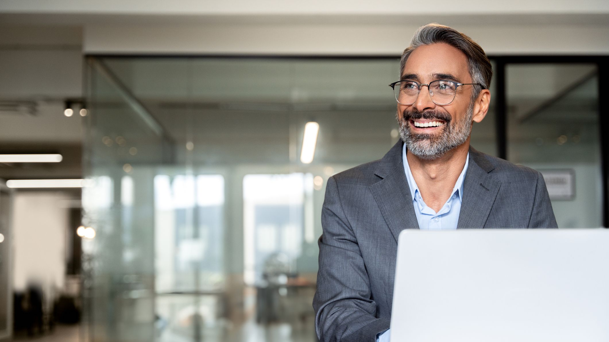 Portrait of mature business man or entrepreneur using laptop computer, typing, working in modern office. Middle-age Hispanic smiling handsome businessman entrepreneur.