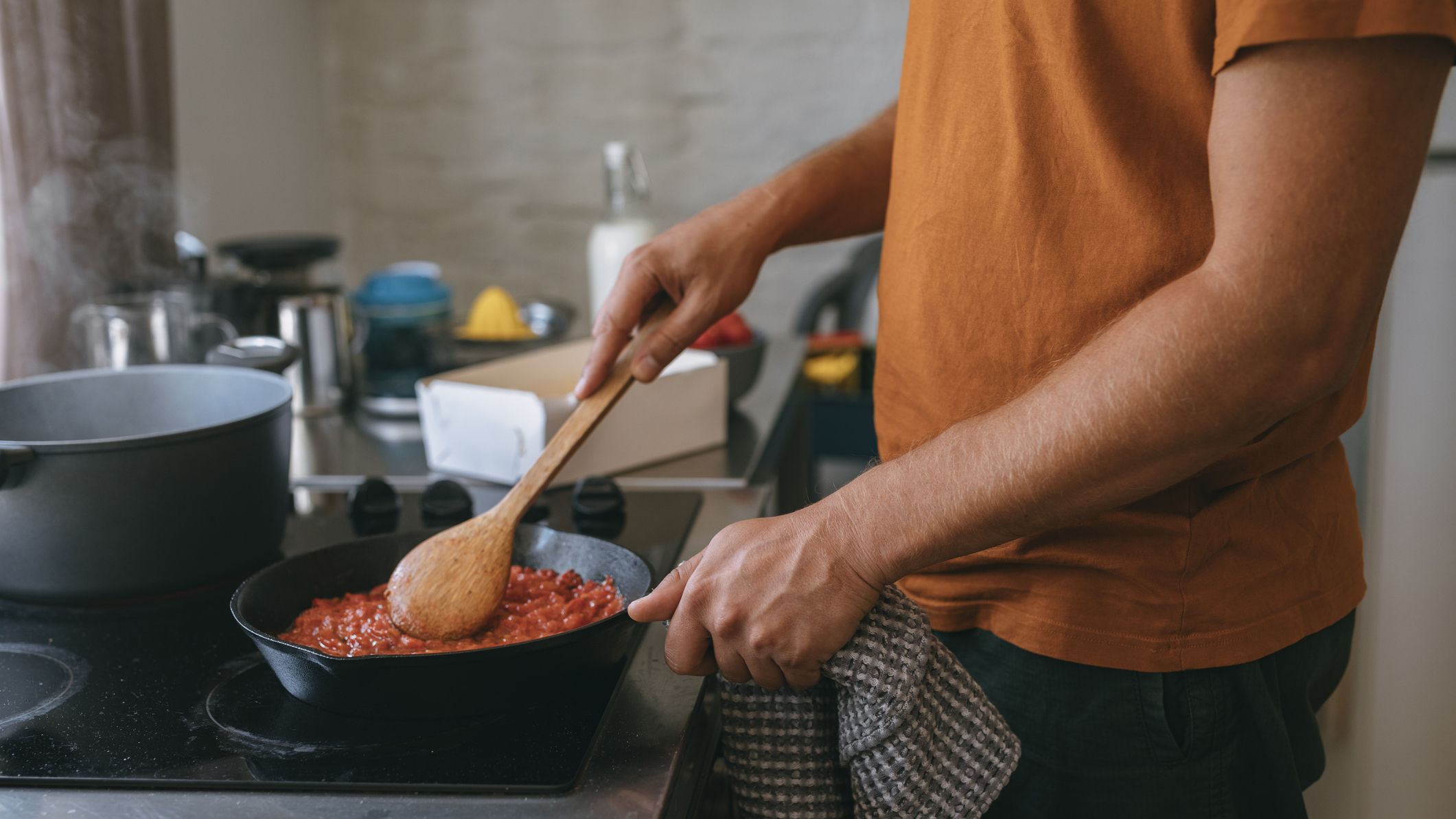 Man stirring pan of tomato sauce on stove with a wooden spoon