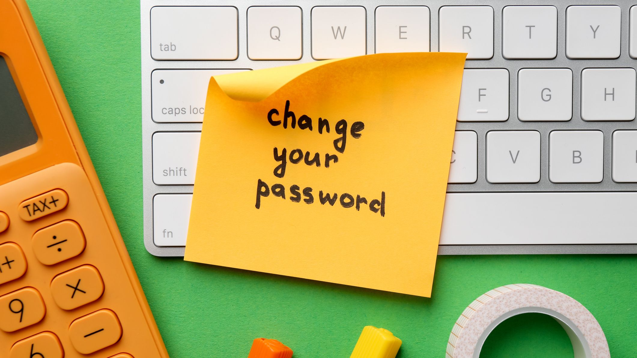 A post it note with the phrase "Change Your Password" written on it surrounded by keyboard and calculator.
