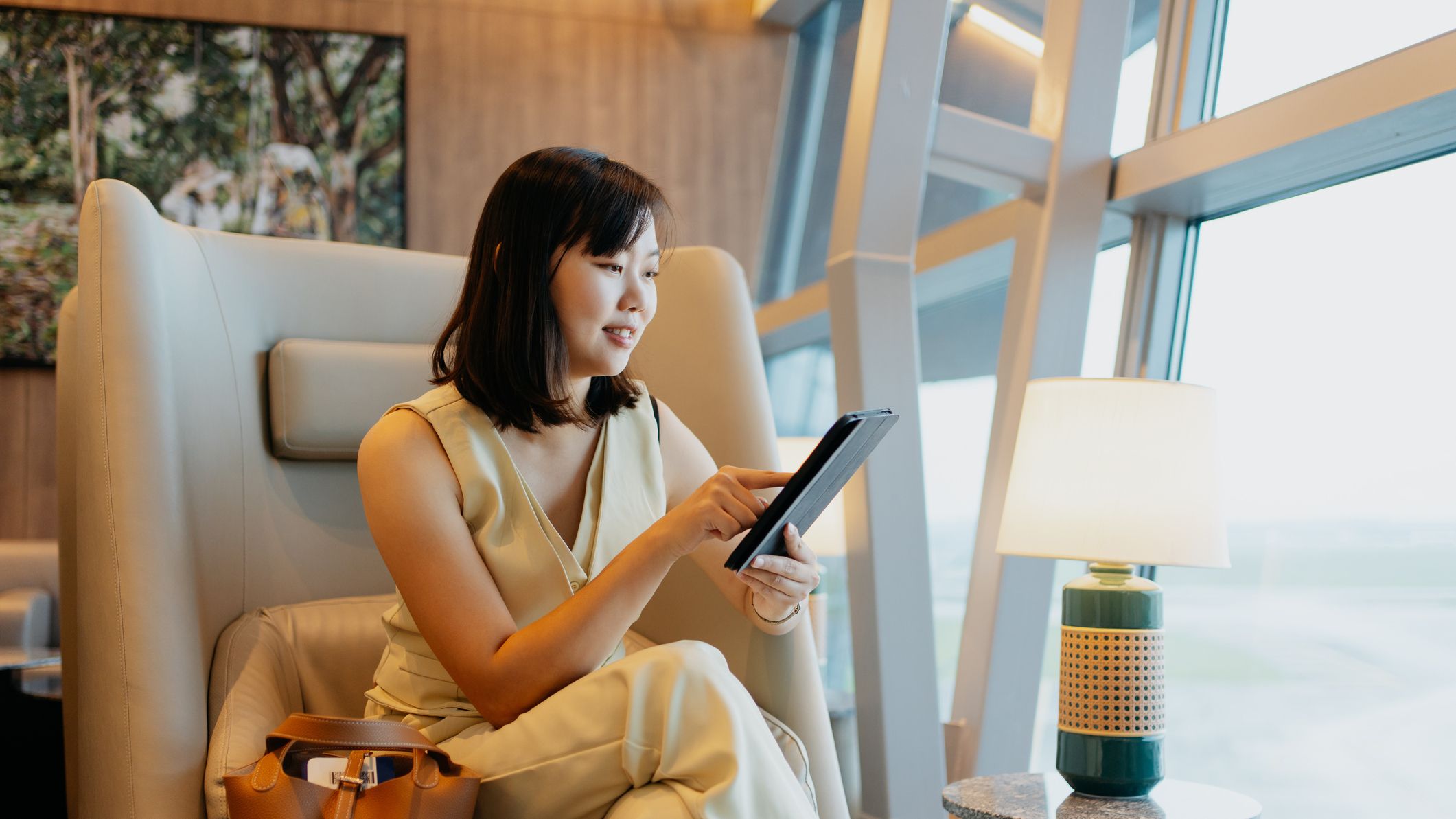 A business woman relaxes in an airport lounge with a capuccino and a tablet computer.