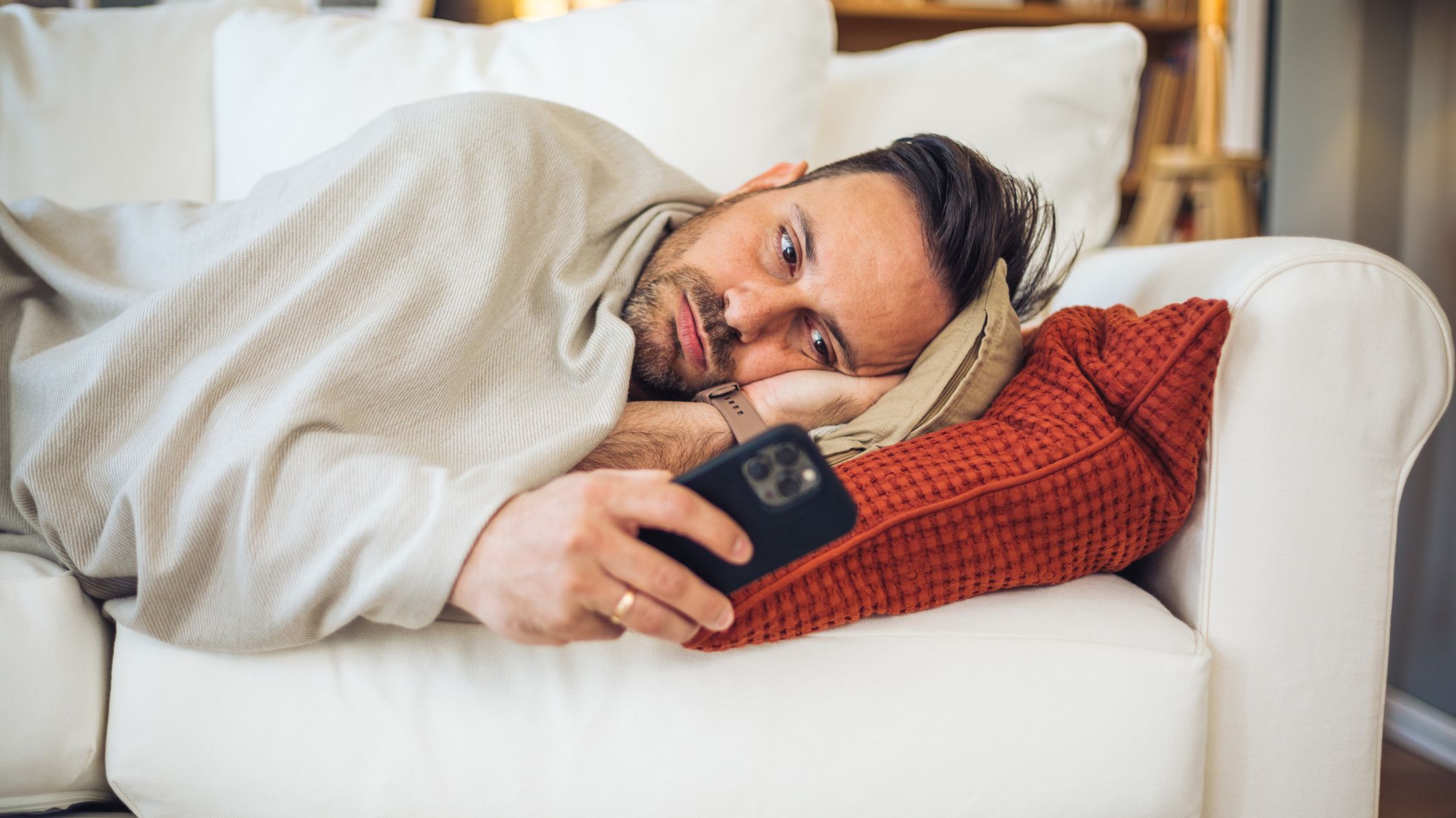 Bored man lying on sofa using smartphone at home.