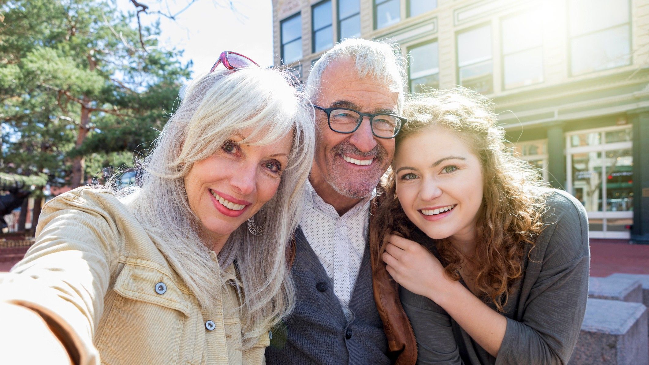 Attractive grandparents smile with their granddaughter outside. The granddather holds a coffee cup.