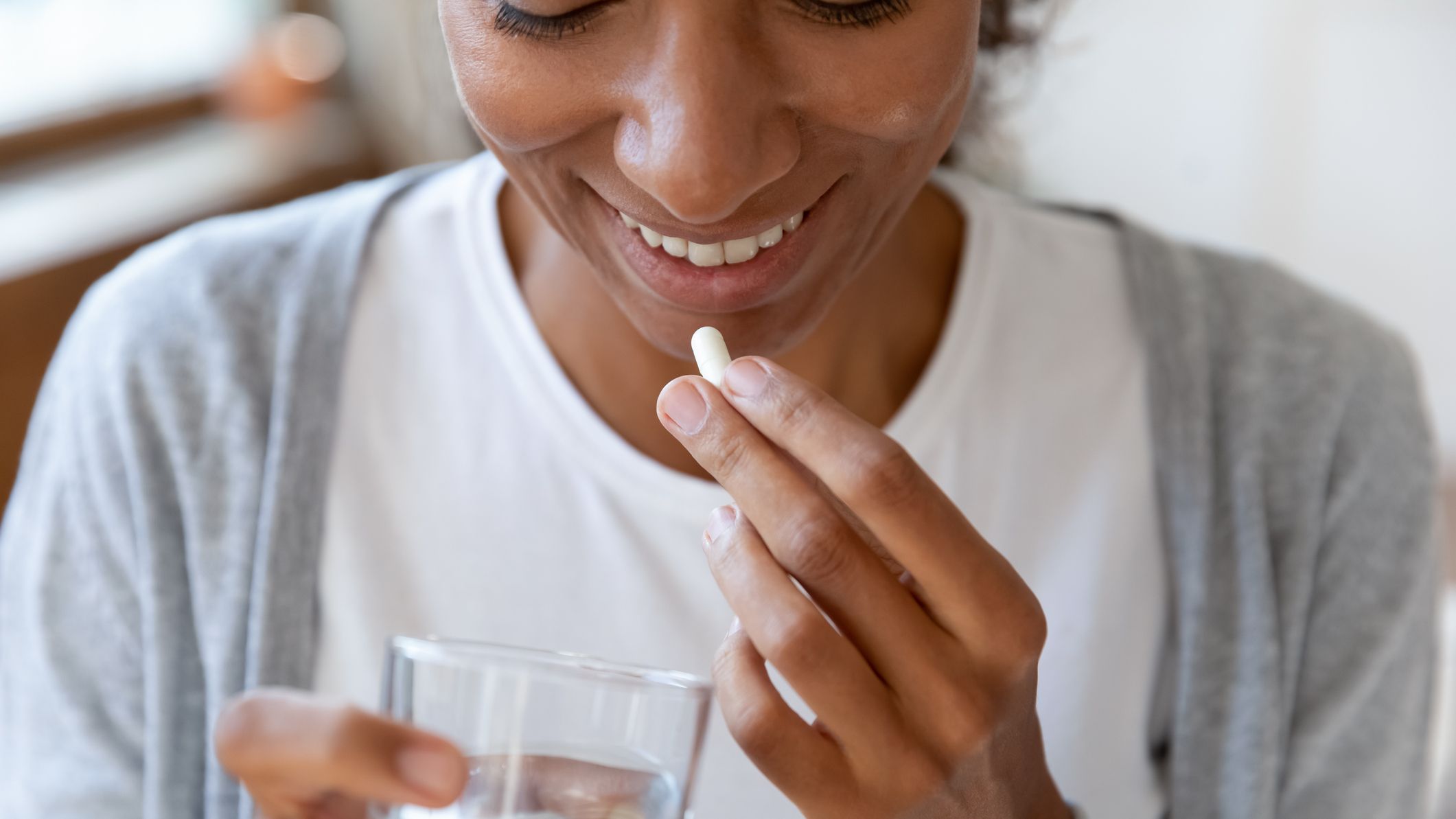 Woman holding a glass of water brings a pill towards her lips