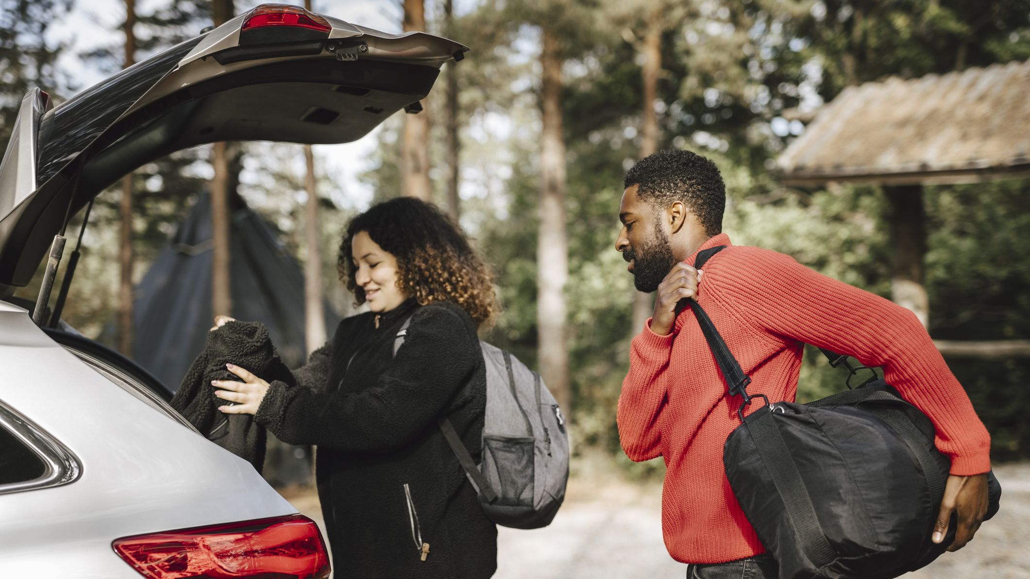 A couple puts luggage in the trunk of a car.