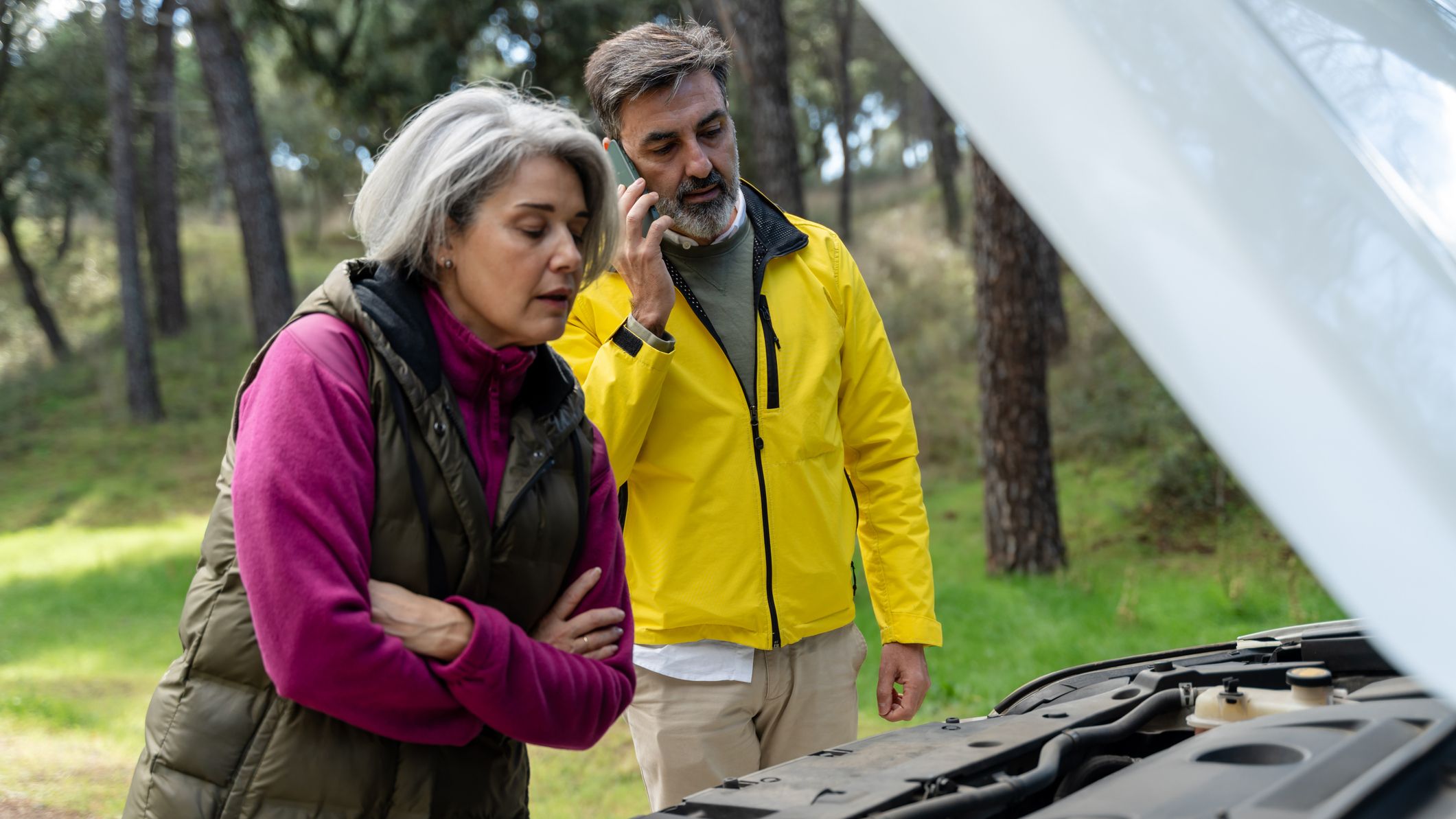 A mature couple experiencing car trouble inspects the engine on the side of the road.