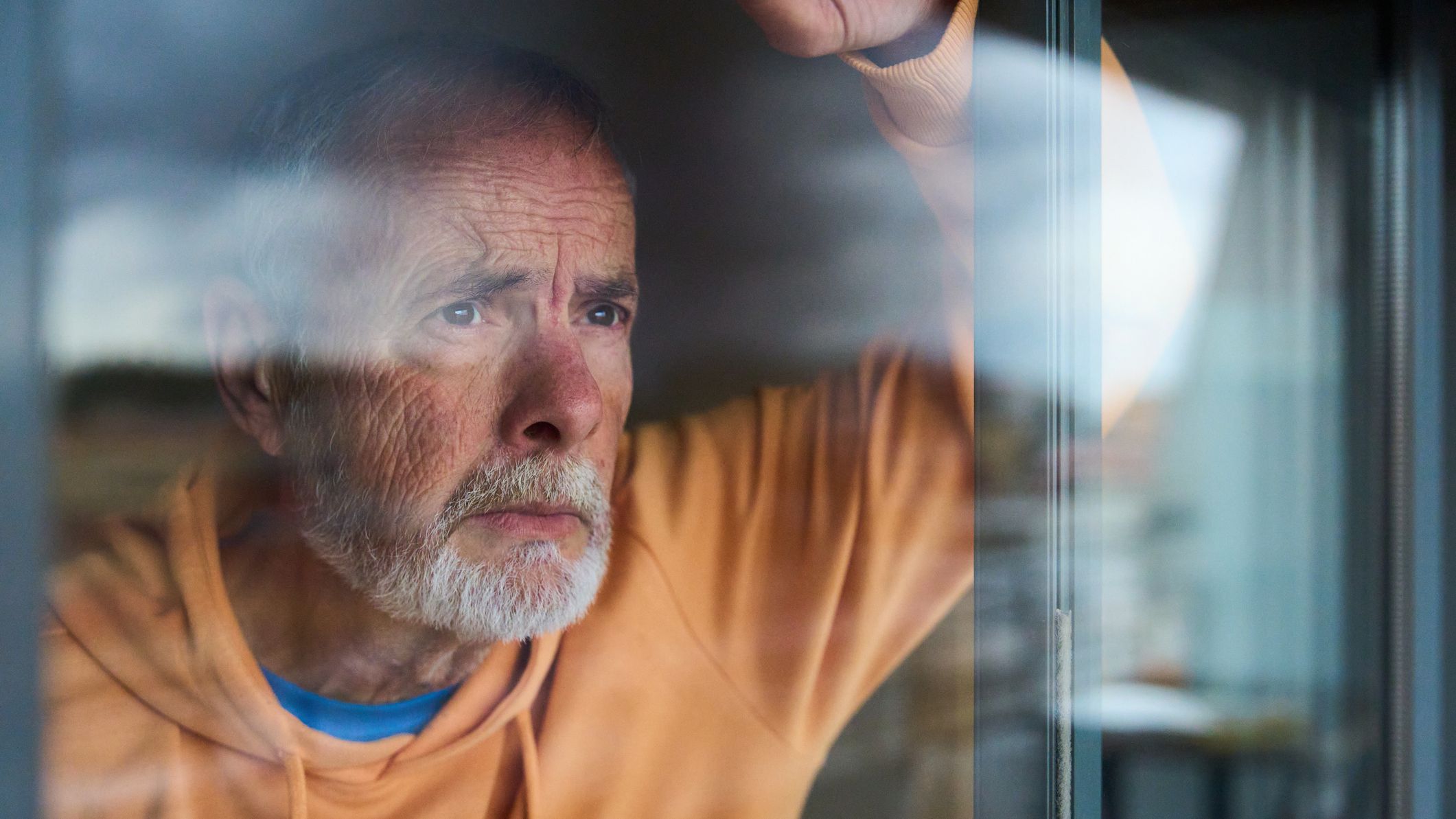 Pensive senior man gazing through the window, wearing a worried expression.