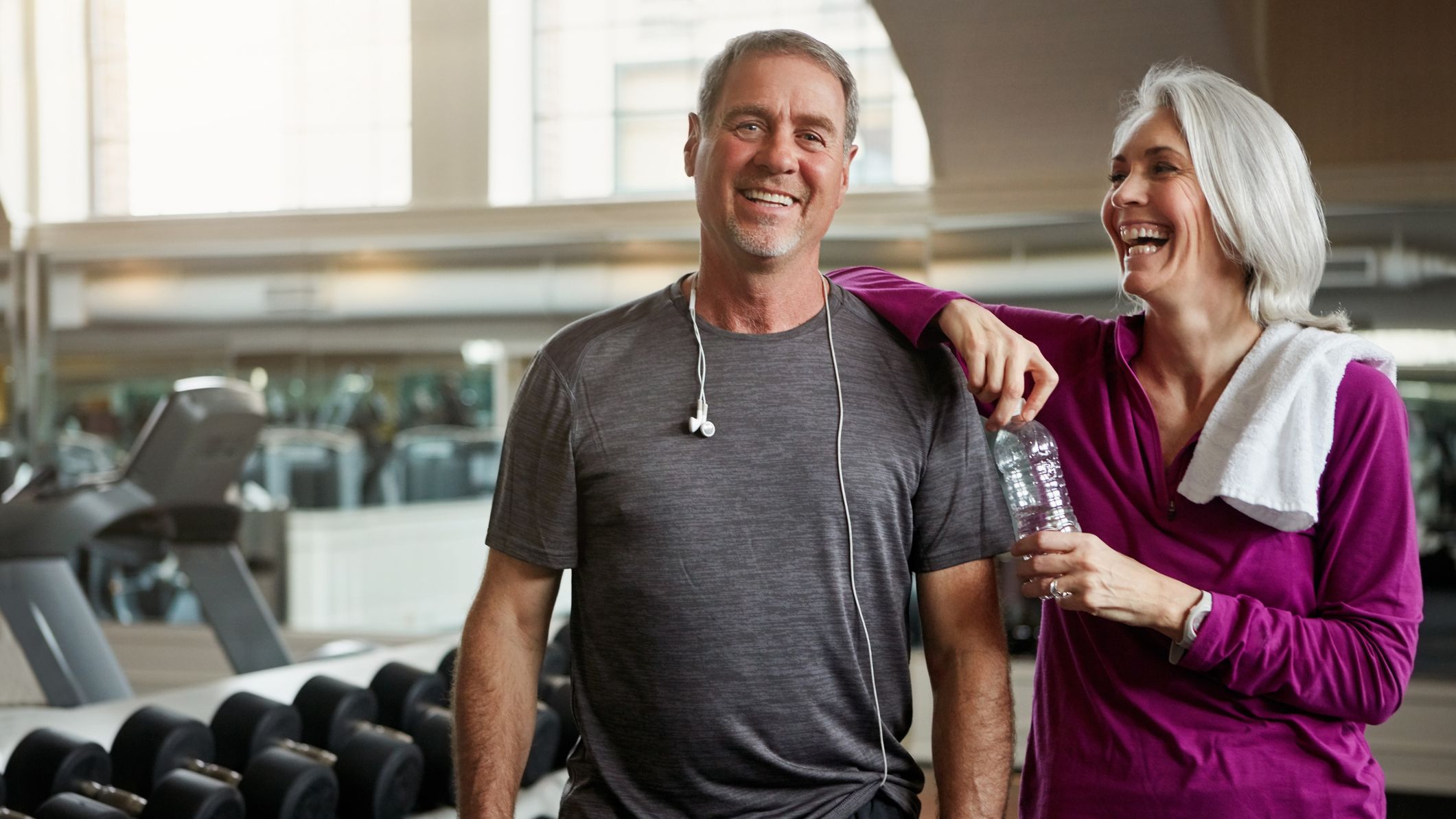 Shot of a senior married couple laughing and taking a break from their workout at the gym.