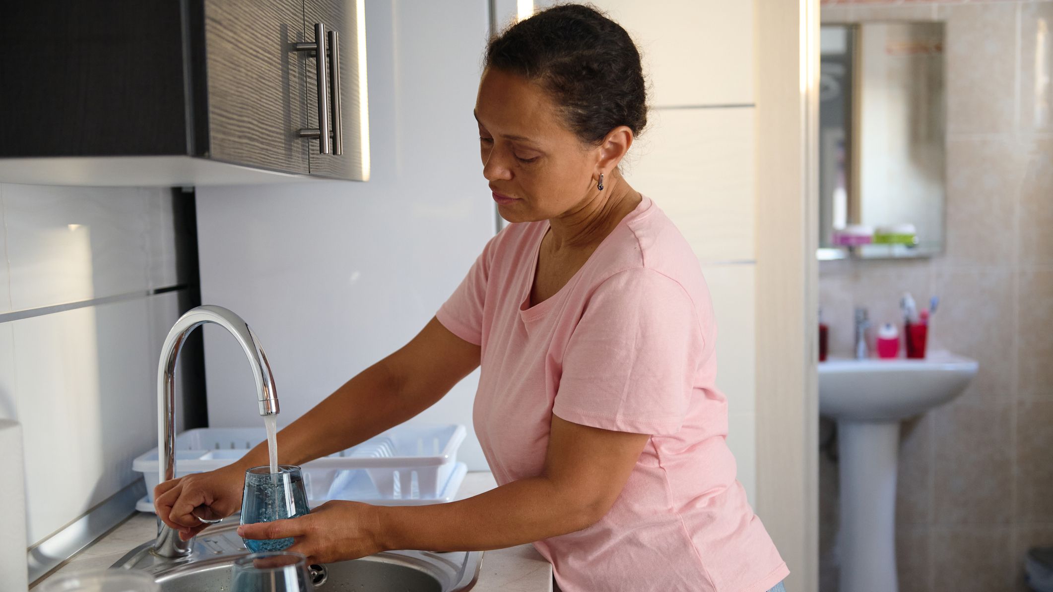 Woman fills up glass with water from a kitchen tap