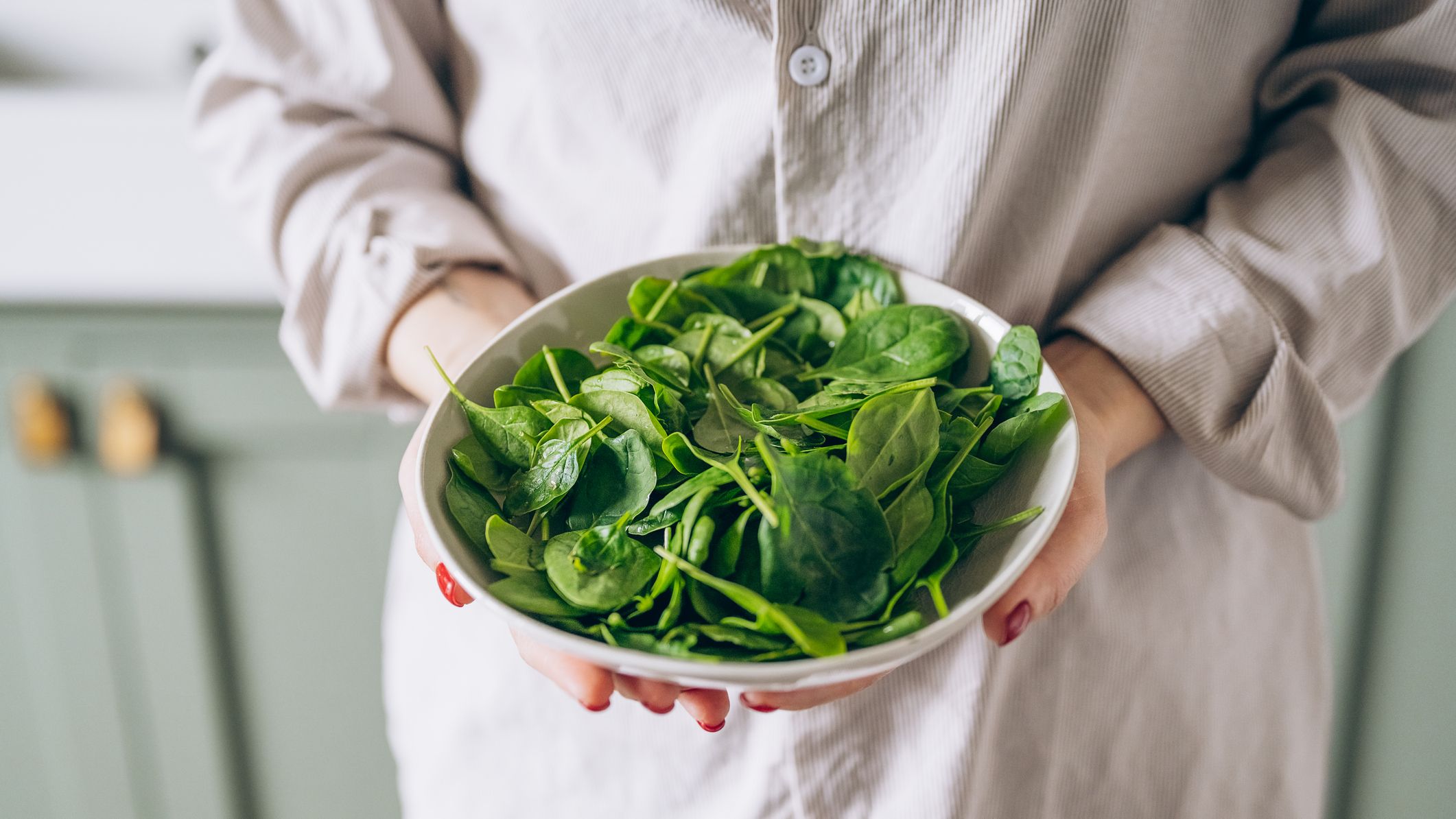 Person holding a bowl of spinach in both hands