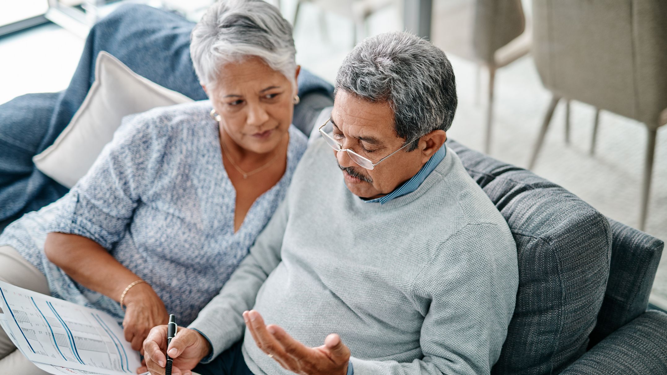 A senior couple discusses their finances while sitting on the couch.