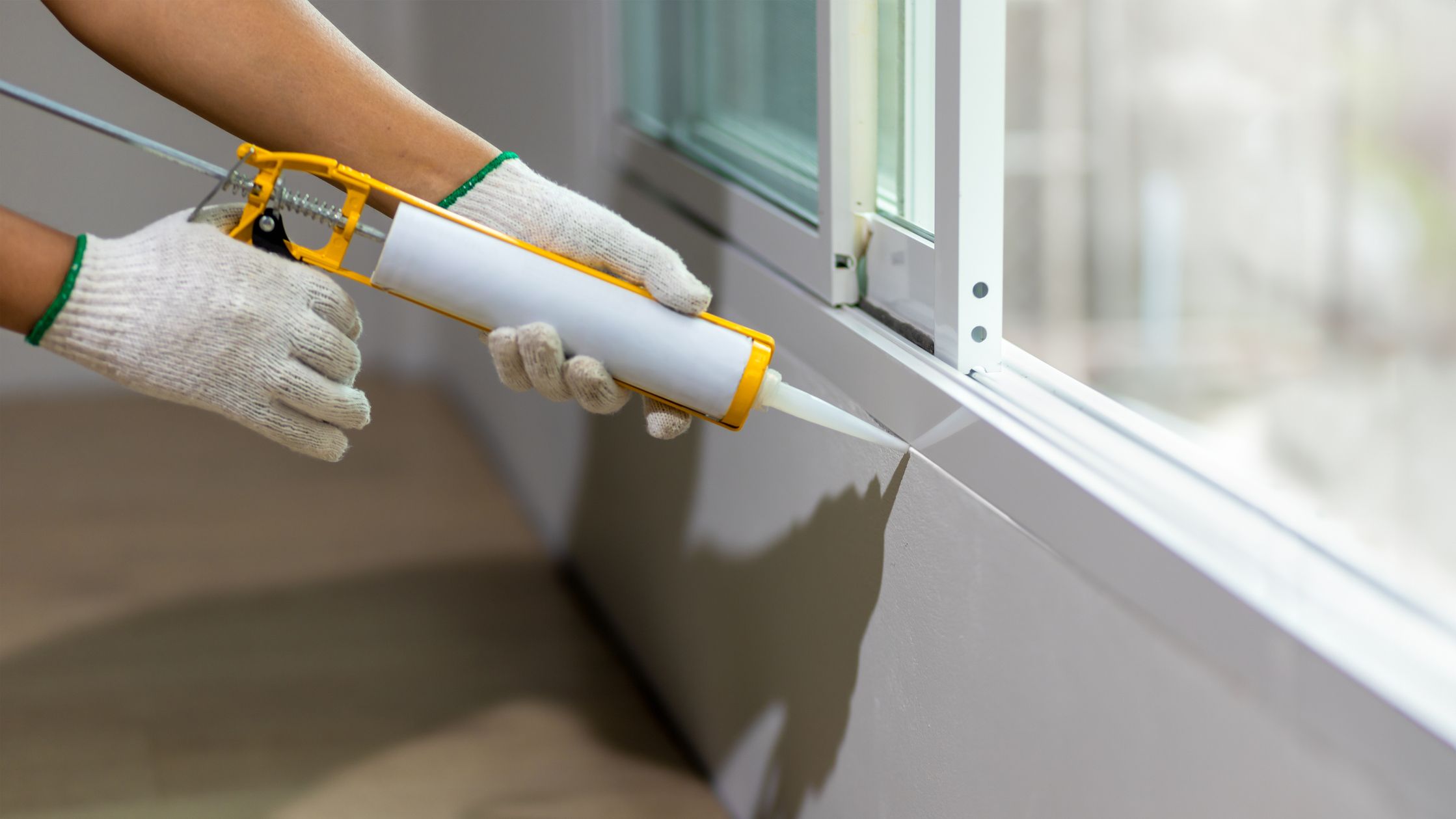 Someone's hands using silicone sealant caulk on the window frame.