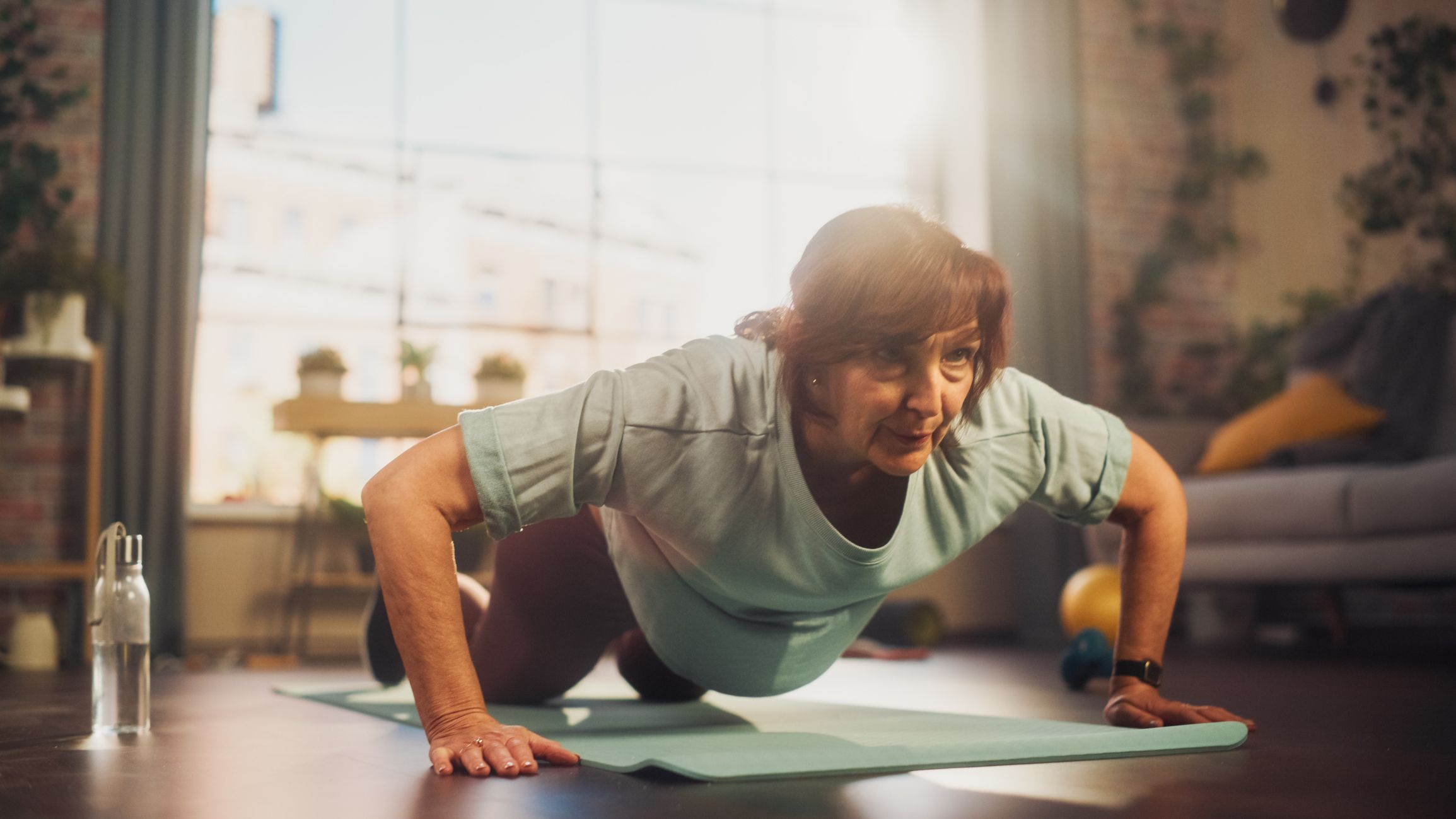 A senior woman doing a push-up on her knees in a domestic setting