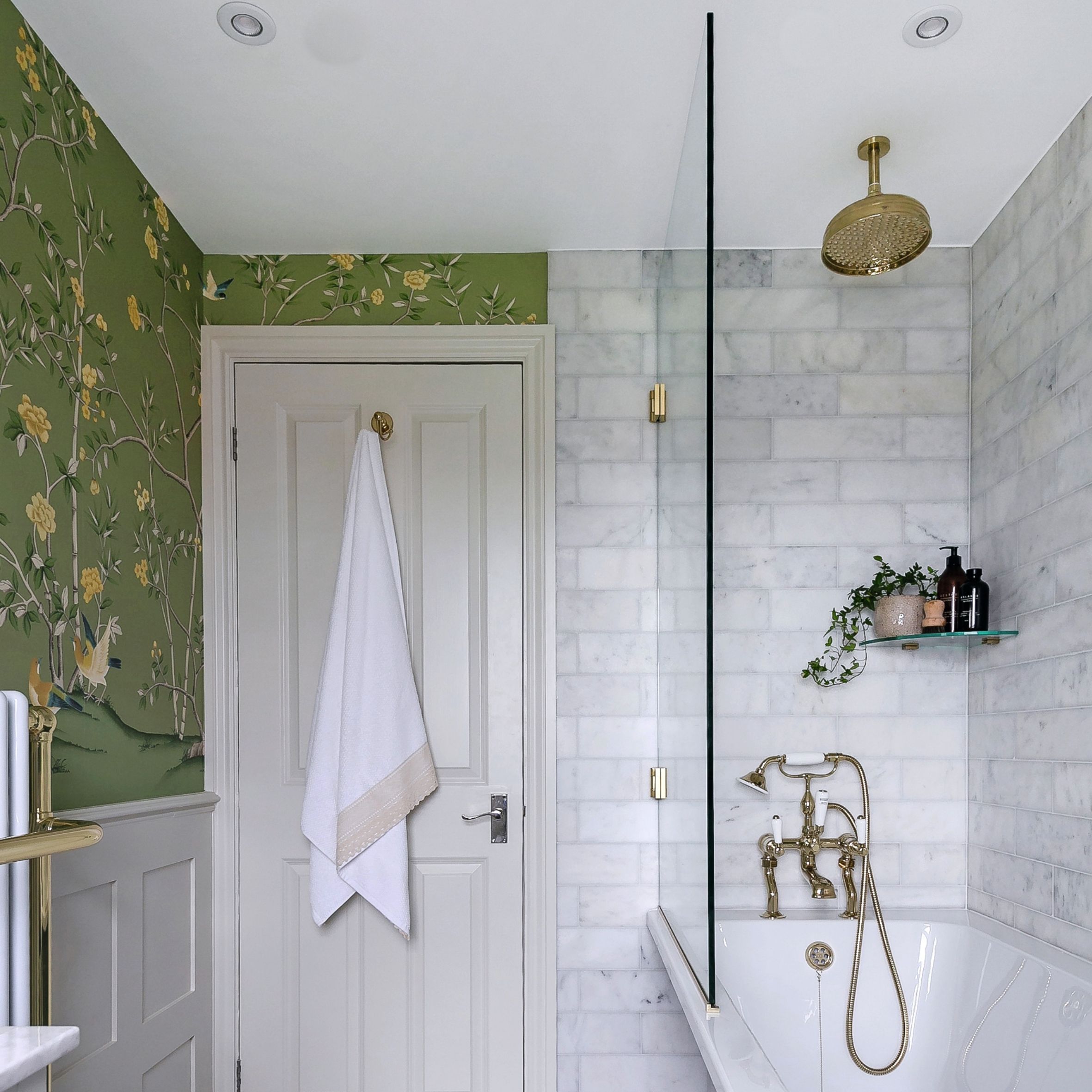 Bathroom view to door, green wallpaper, marble wall tiles, gold rainfall shower head over tub and white door