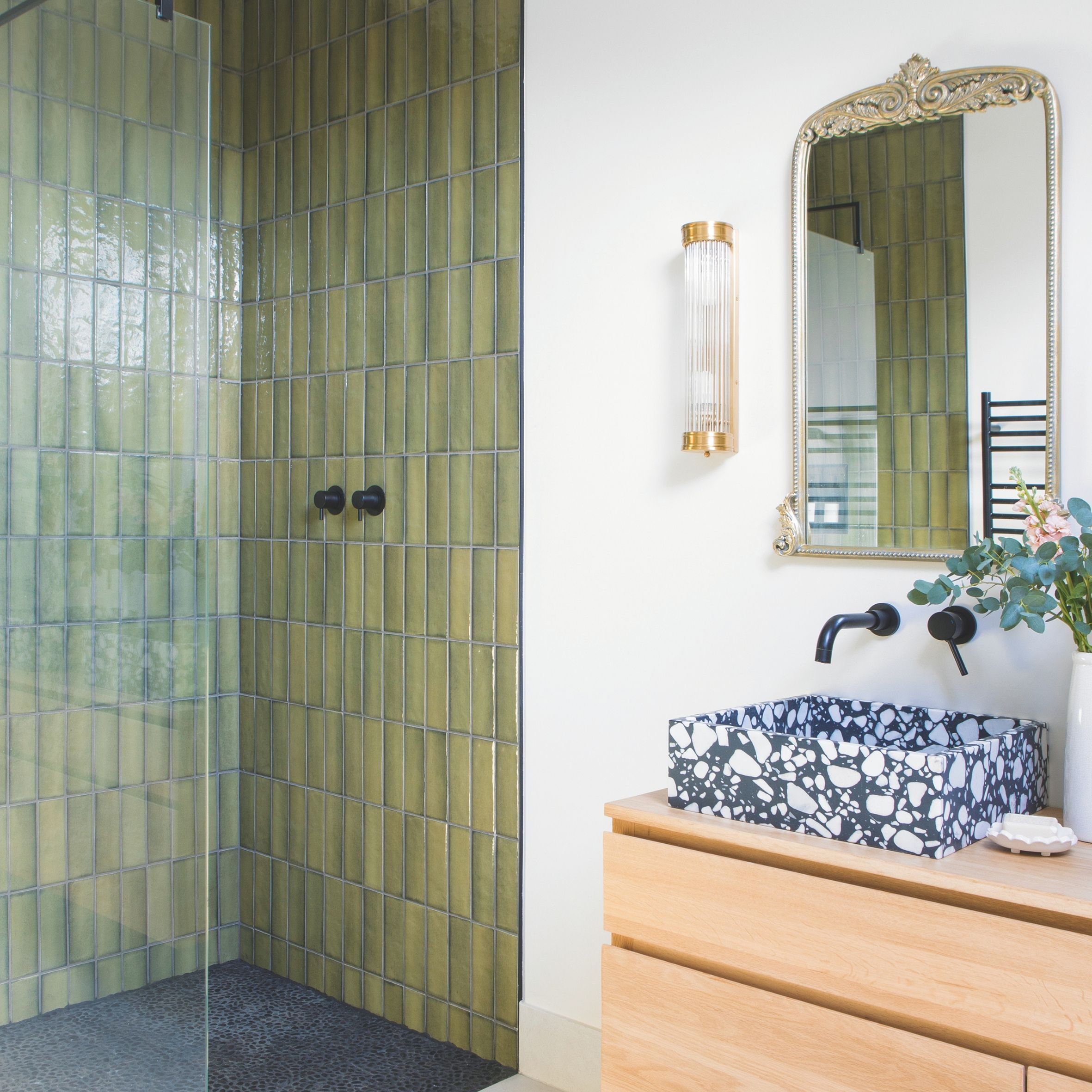Green tiled walk in shower beside marble bathroom sink