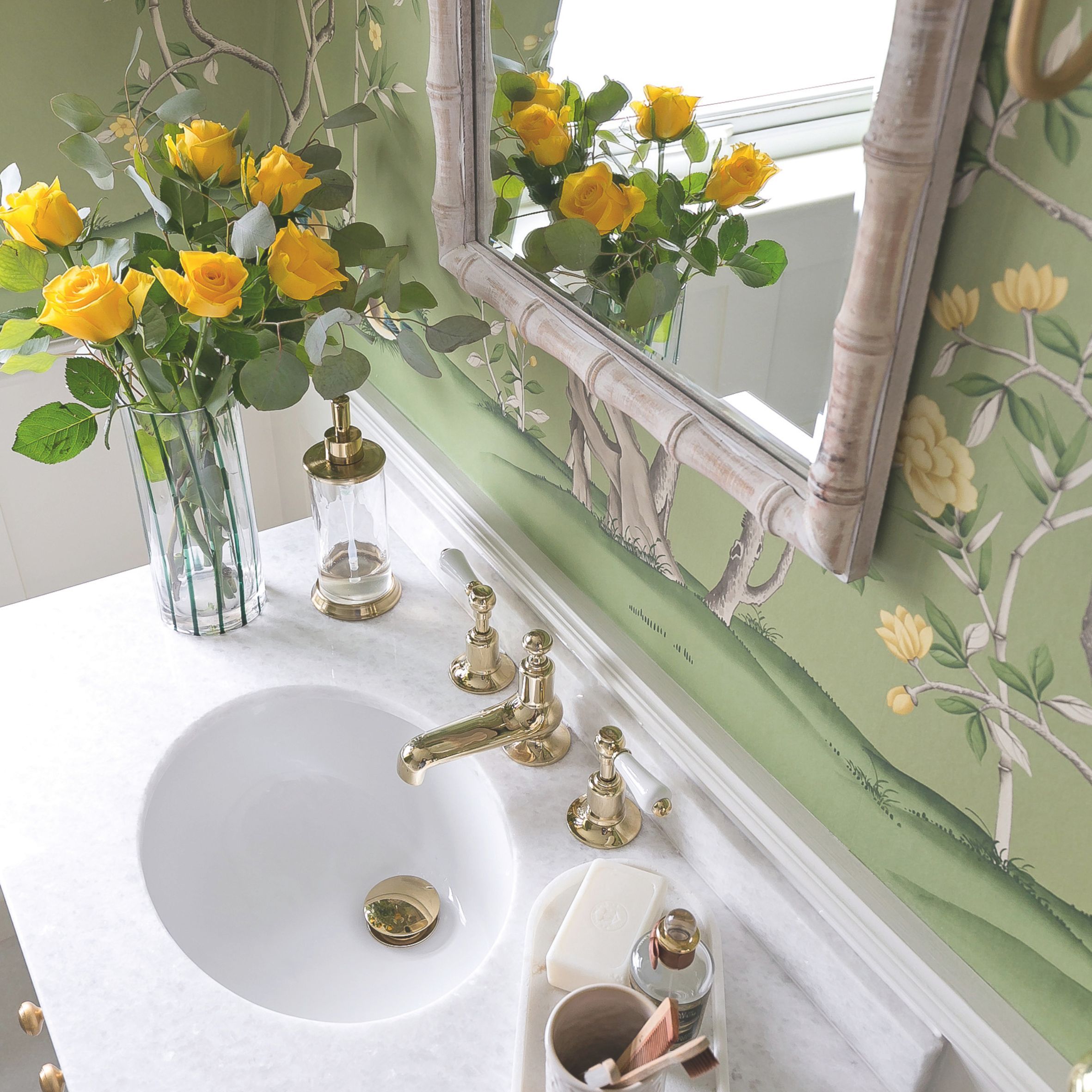 Green wallpapered bathroom with bamboo mirror, marble vanity and yellow roses