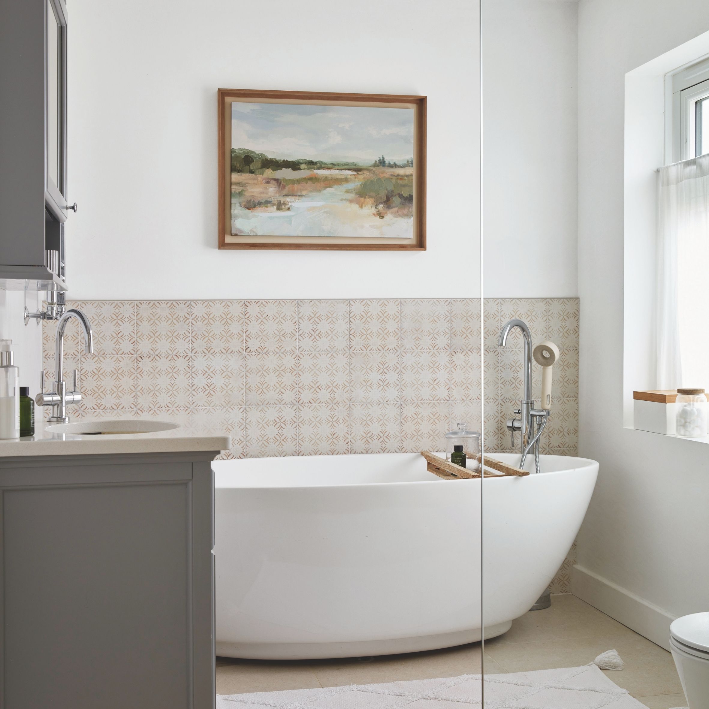 En suite bathroom with grey unit, freestanding tub, pink subtle wall tiles and painting on the wall