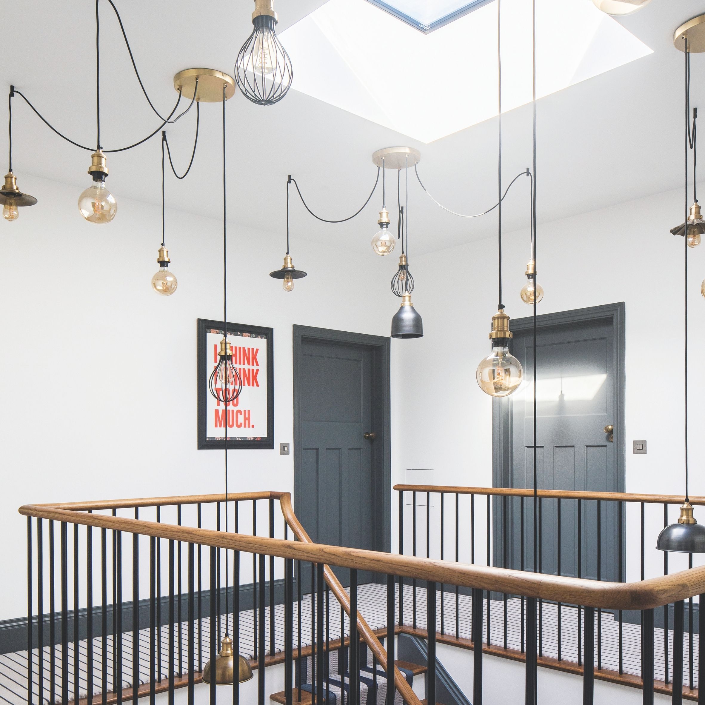large landing aren with wooden and black staircase, black doors and lots of hanging lights on ceiling