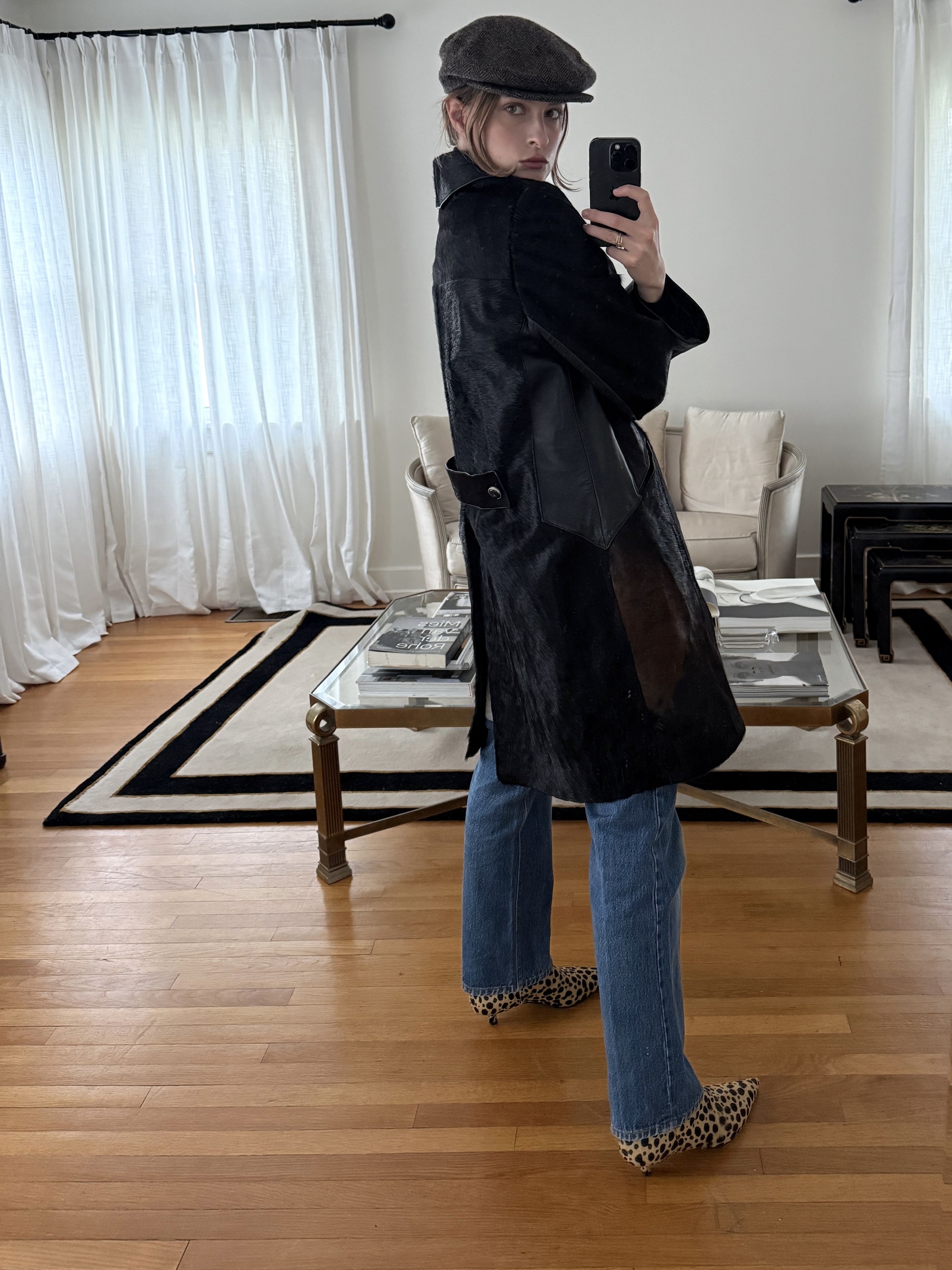Christie Tyler taking a selfie wearing a black jacket, jeans, and leopard print shoes, with a newsboy cap