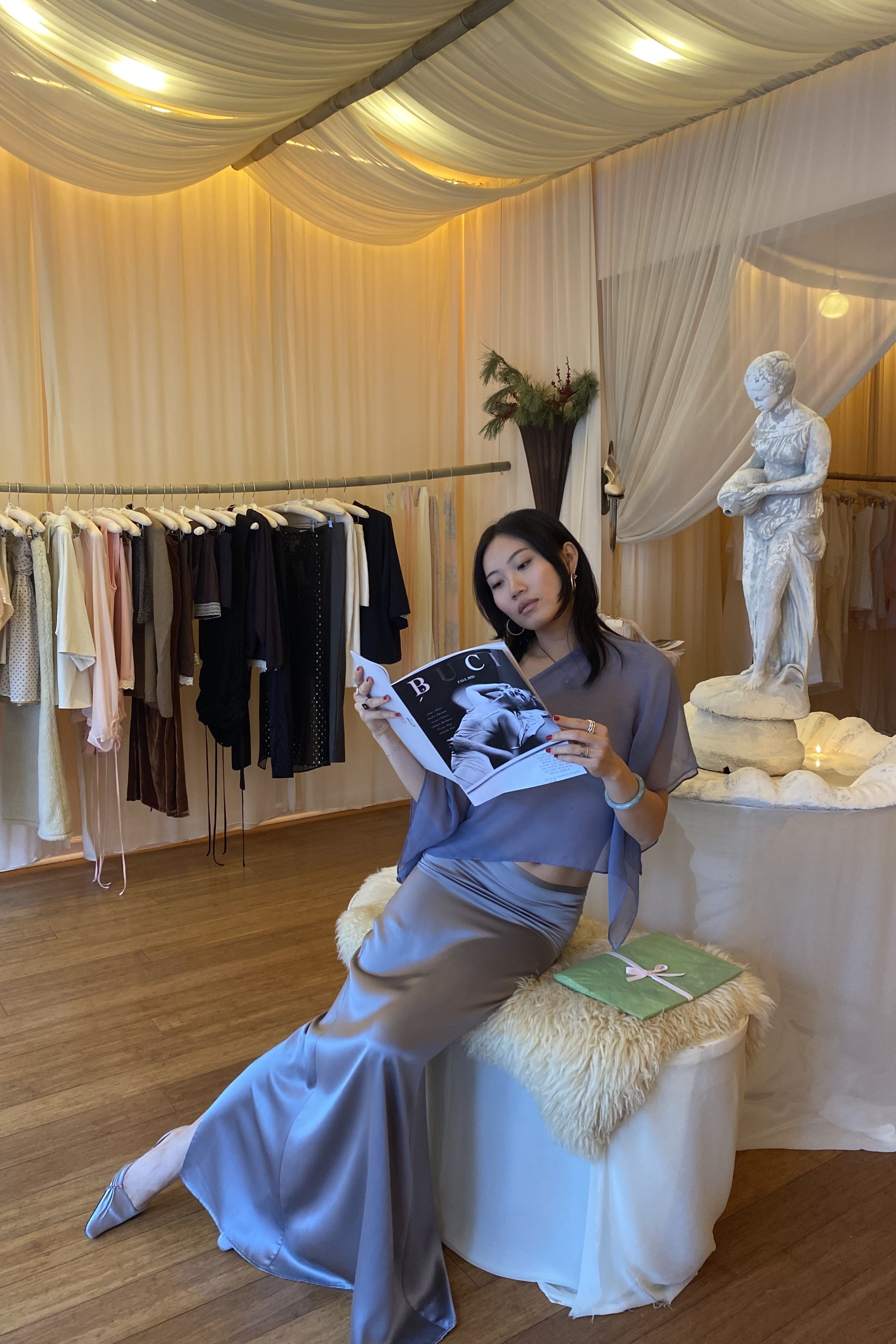 Vivian Li reading a magazine in a boutique wearing a silk skirt and top