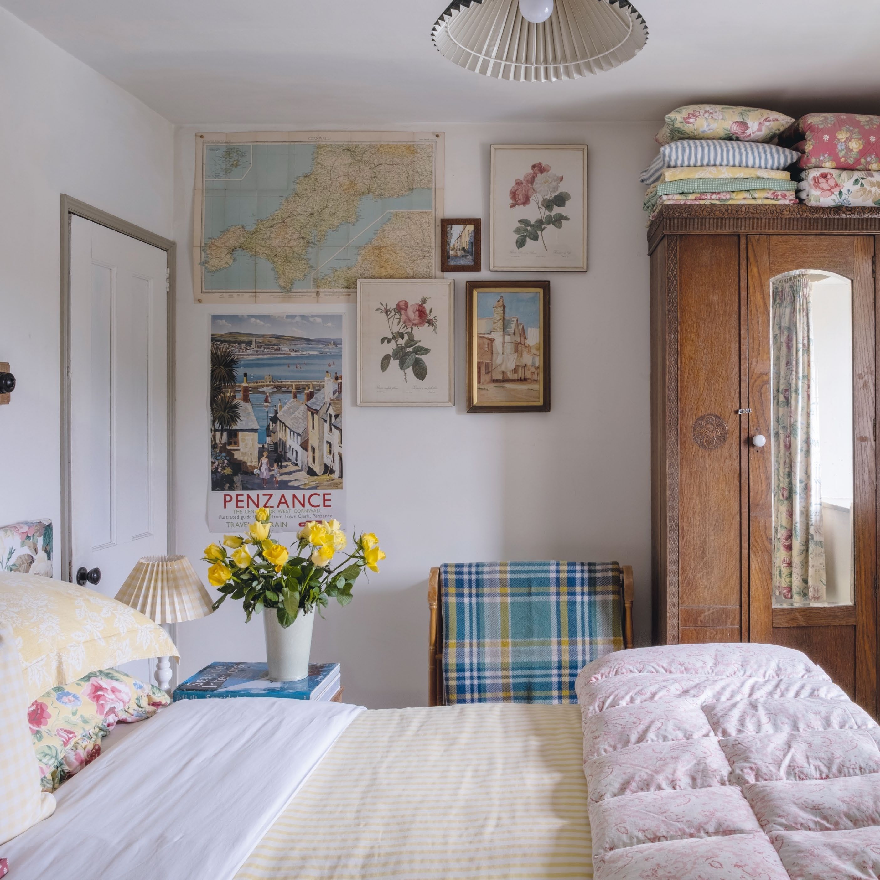 Cottage bedroom with mixed vintage prints on wall, floral bed linen and vintage wardrobe