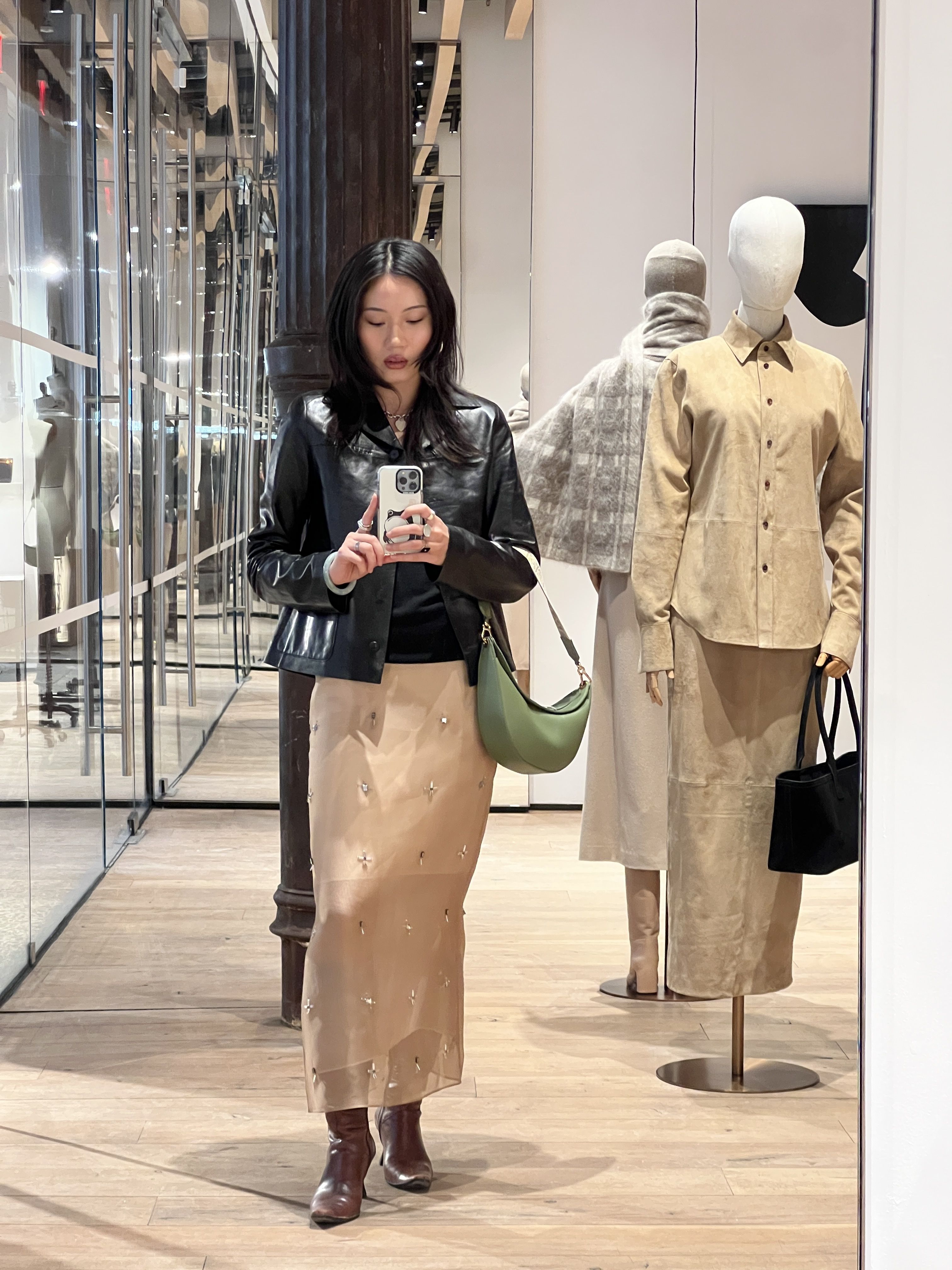 Vivian Li wearing a silk skirt and a black leather jacket while taking a selfie in a store mirror