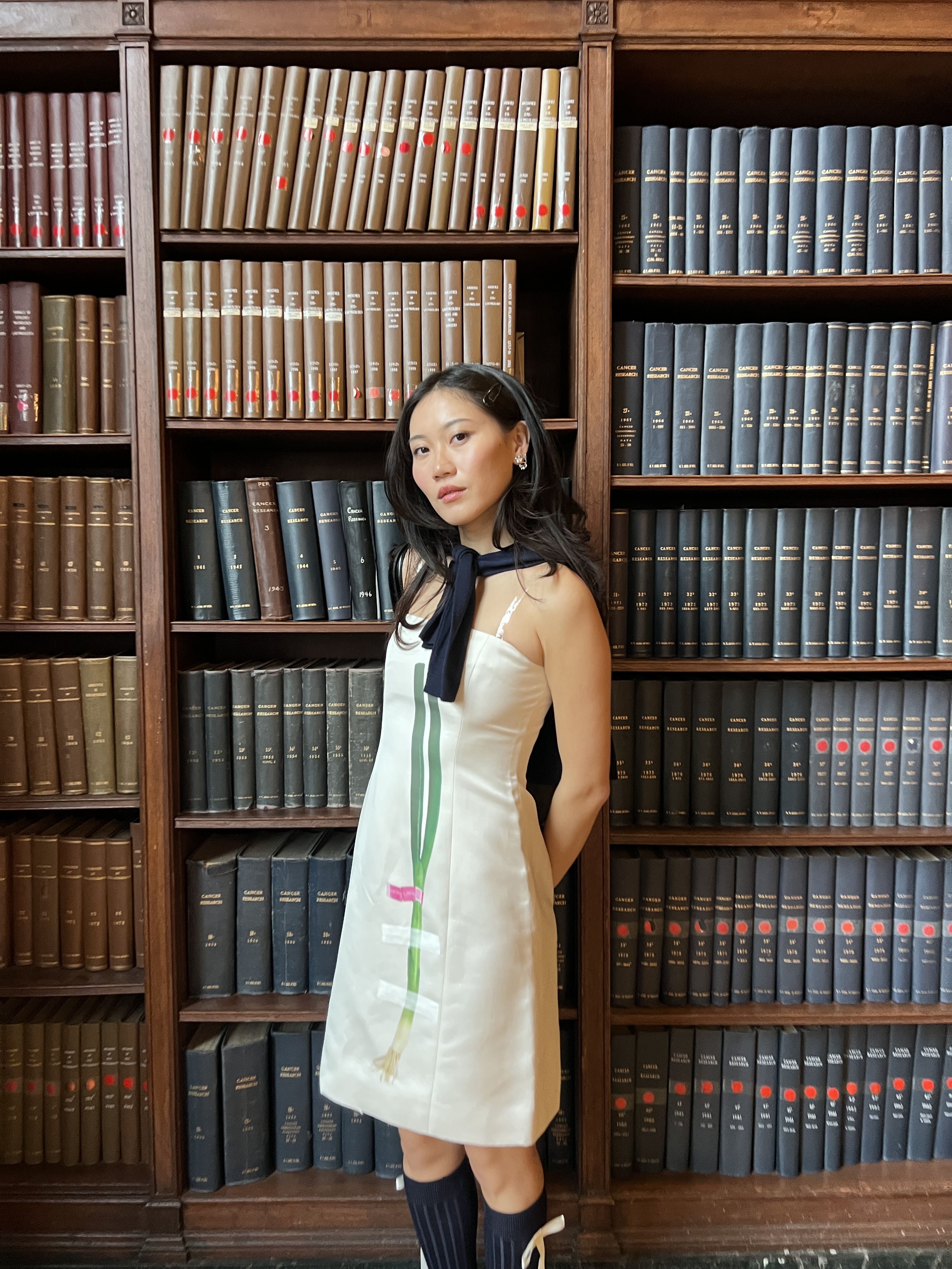 Vivian Li wearing a Sandy Liang dress next to a bookshelf
