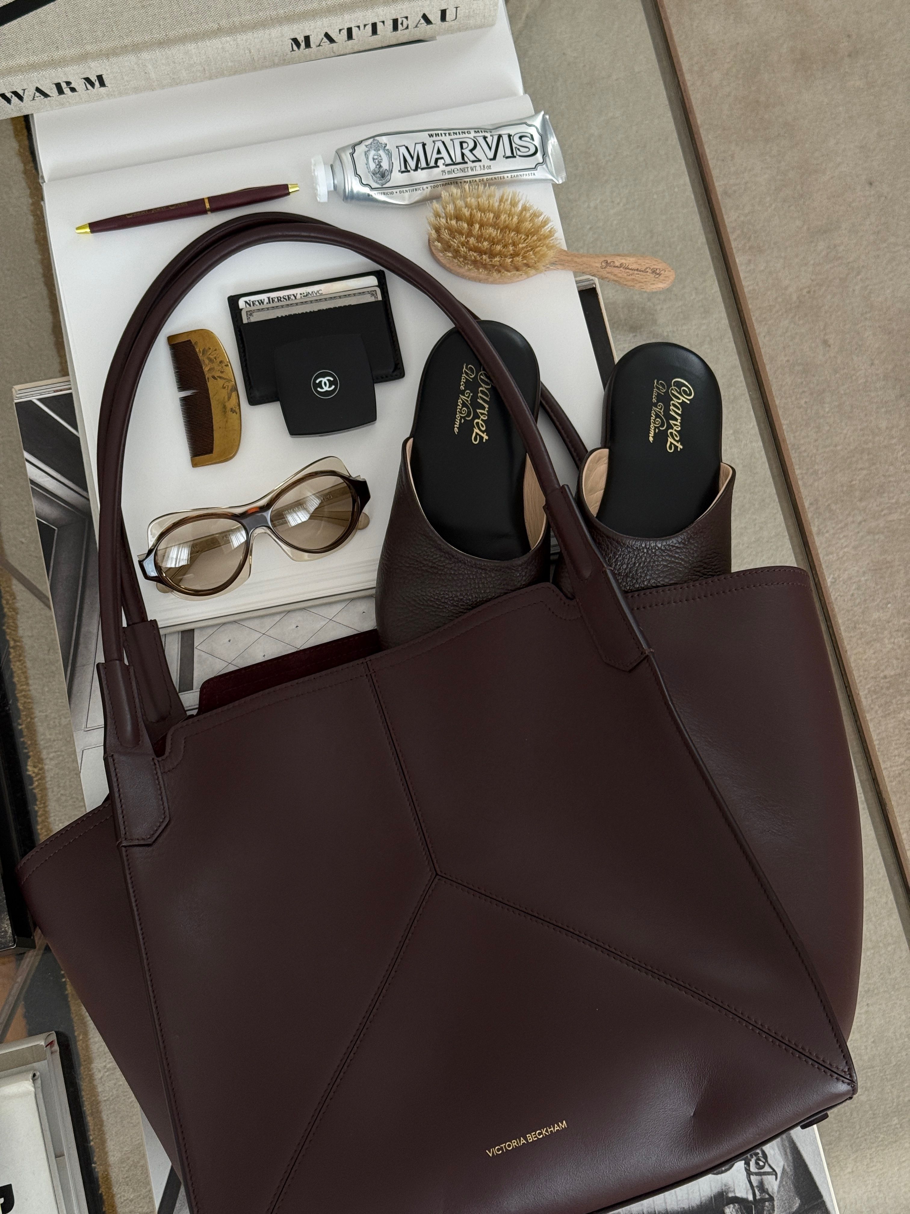 a bag on a table next to a hairbrush, a pair of shoes, a comb, and sunglasses