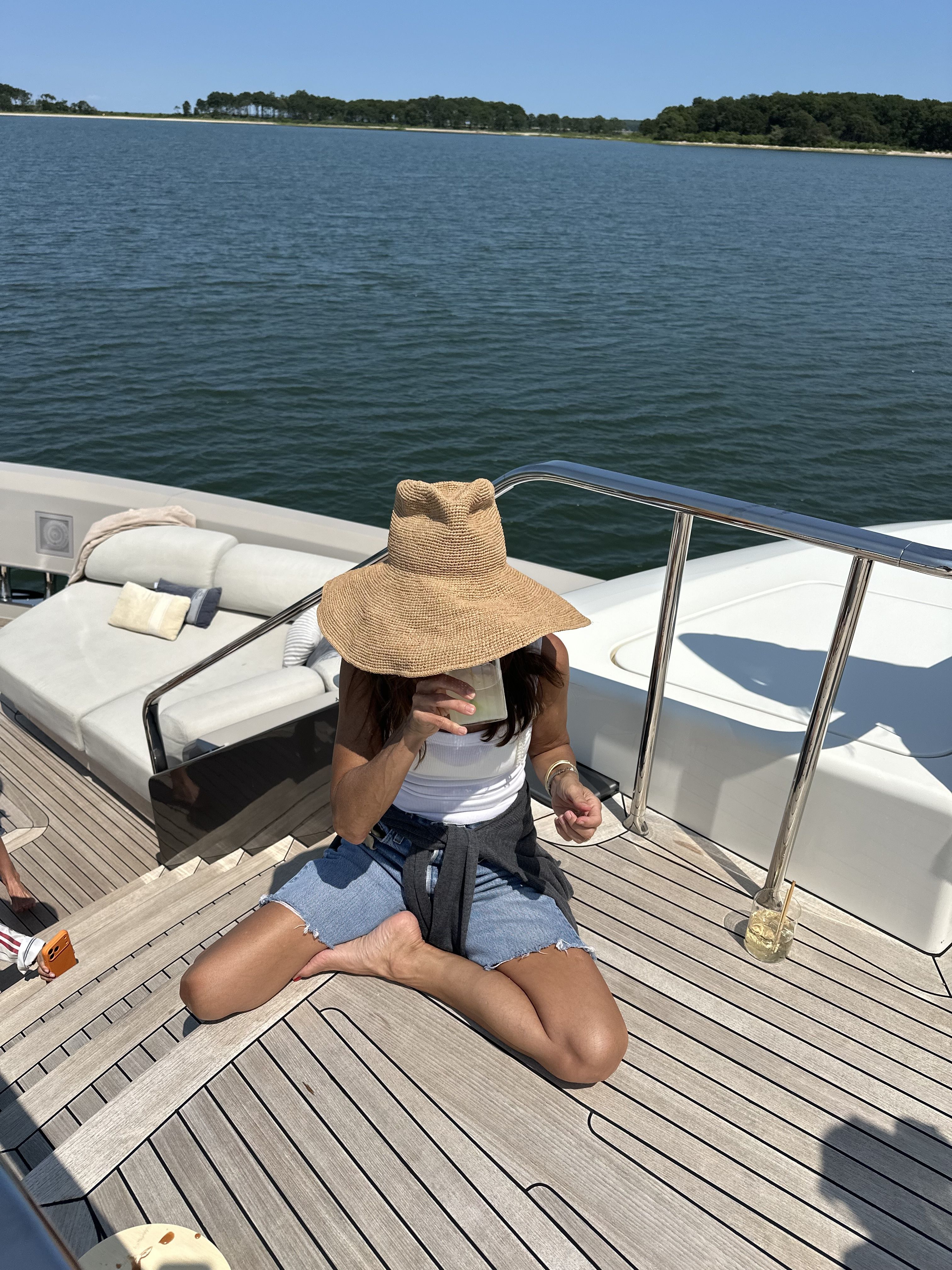 Larissa Mills wears denim shorts with a white top and big straw hat while on a boat