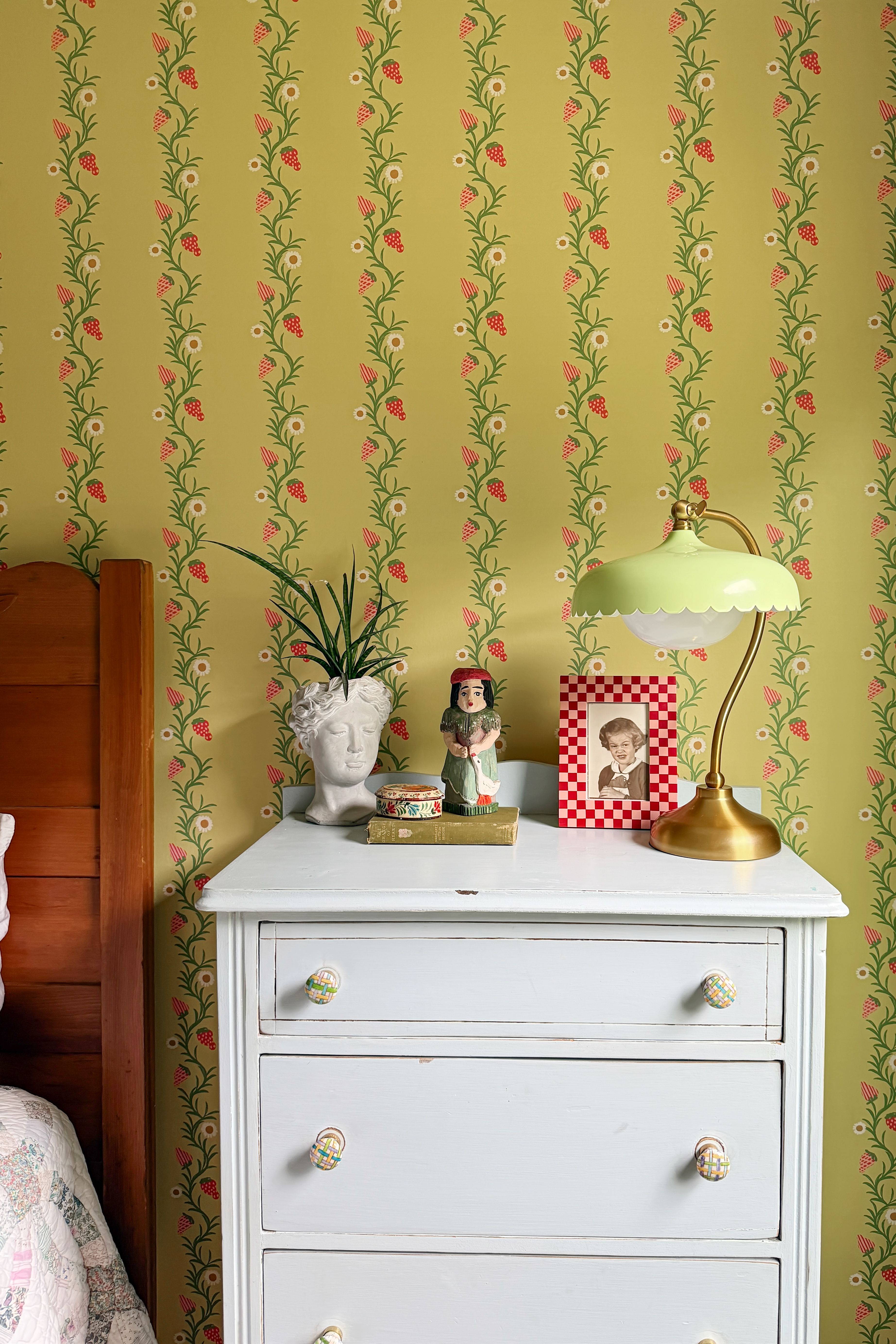 Bedroom featuring a white multi-drawer nightstand displaying various objects and chartreuse floral-motif wallpaper.