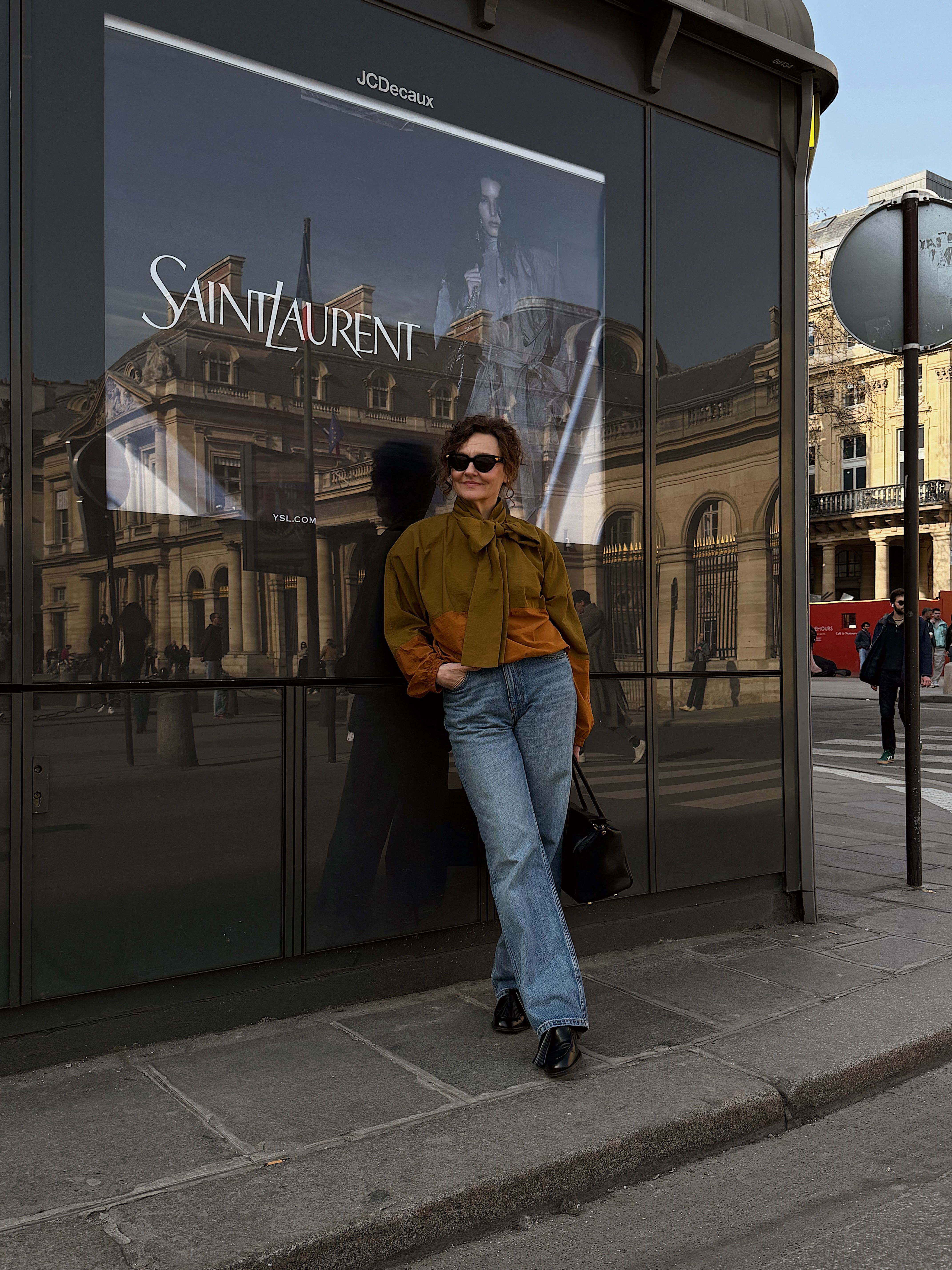Renia Jazdzyk wears a bow-embellished windbreaker with jeans and sunglasses, posing in front of Saint Laurent in Paris