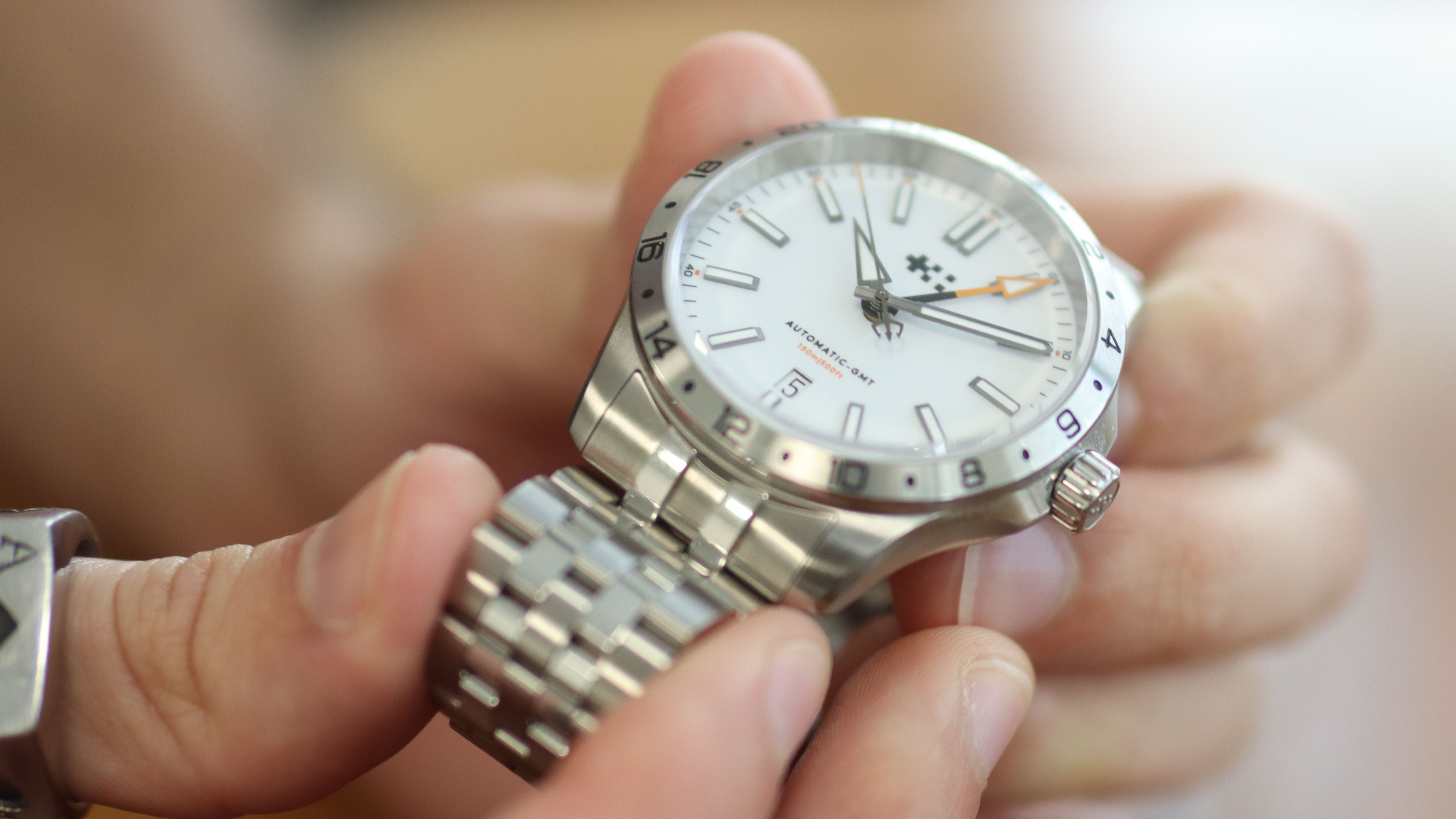 The Christopher Ward Consort bracelet in use on a C63 Sealander GMT, against a wooden background
