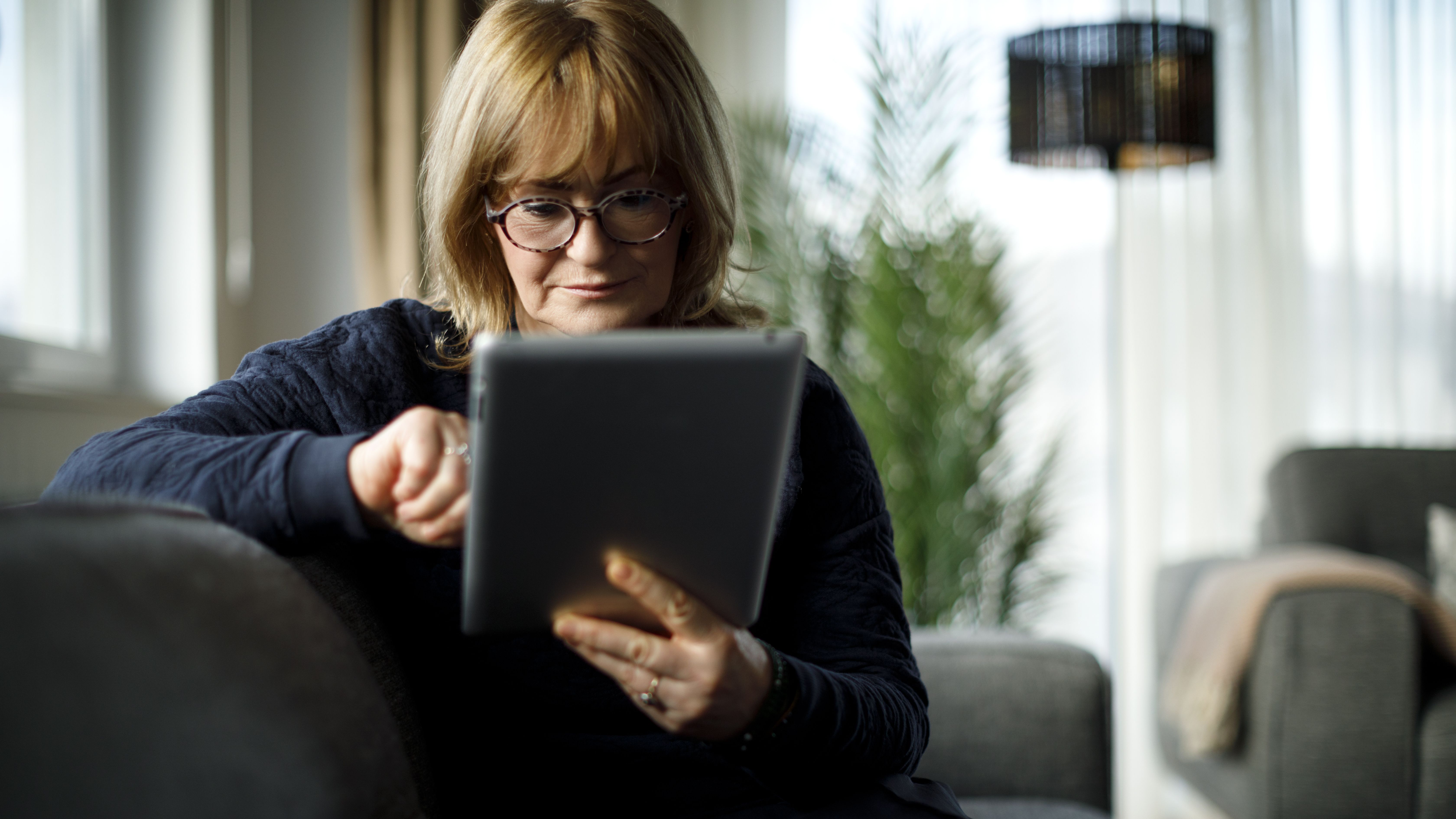 A senior woman relaxes on the couch while reading an ereader.