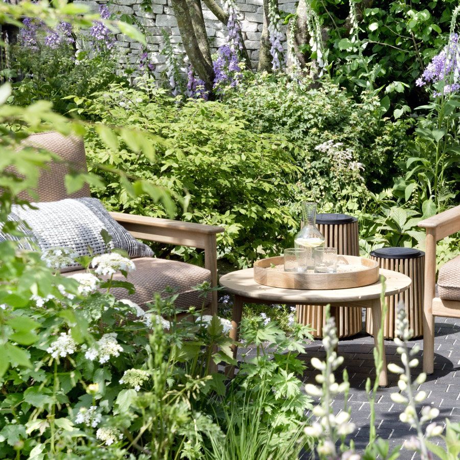 Packed flower beds around a paved seating area with a two chairs and a table