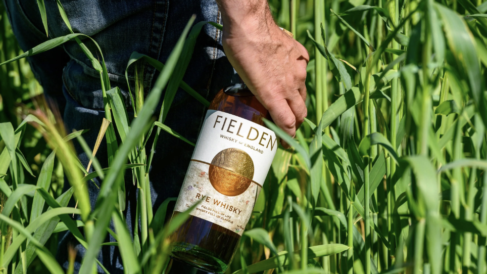 an image of the Fielden Rye Whisky being held by a man walking through a grassy field