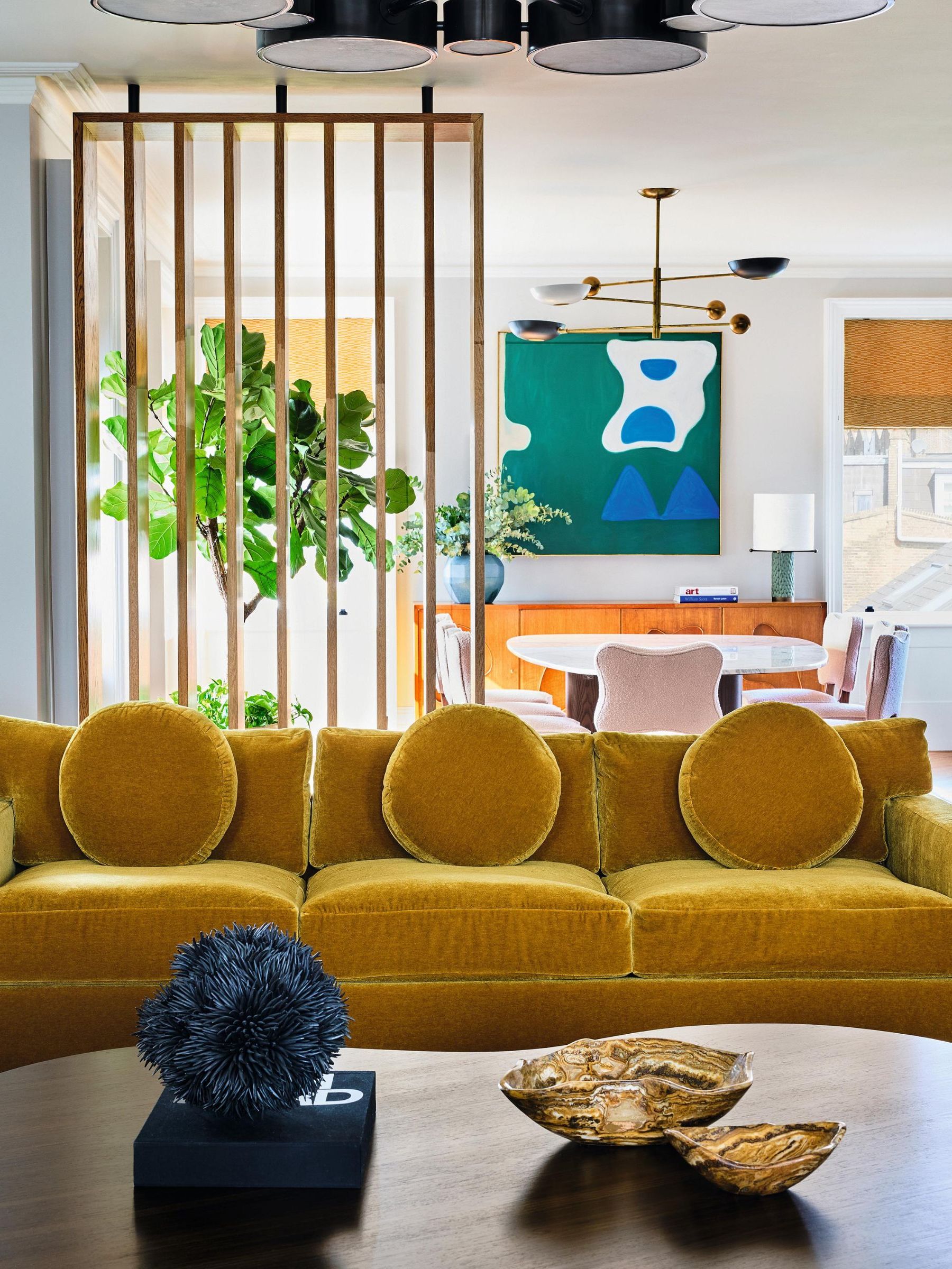 a white living room with wooden dividers, wooden coffee table, mustard velvet couches and abstract art and decor