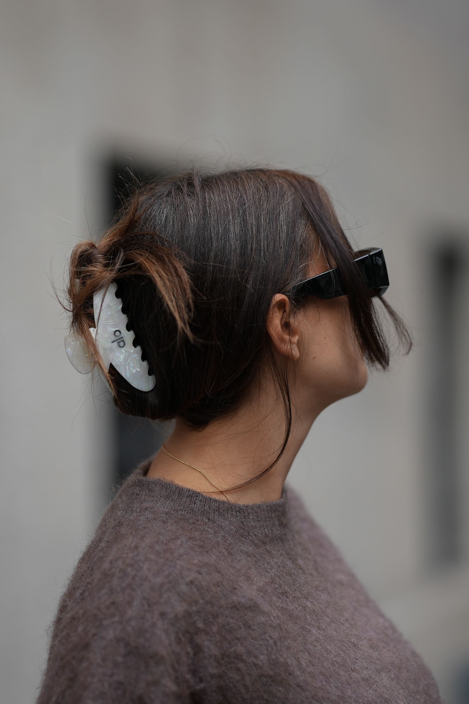 A woman wearing a brown sweater sunglasses and a translucent claw clip in her brown hair