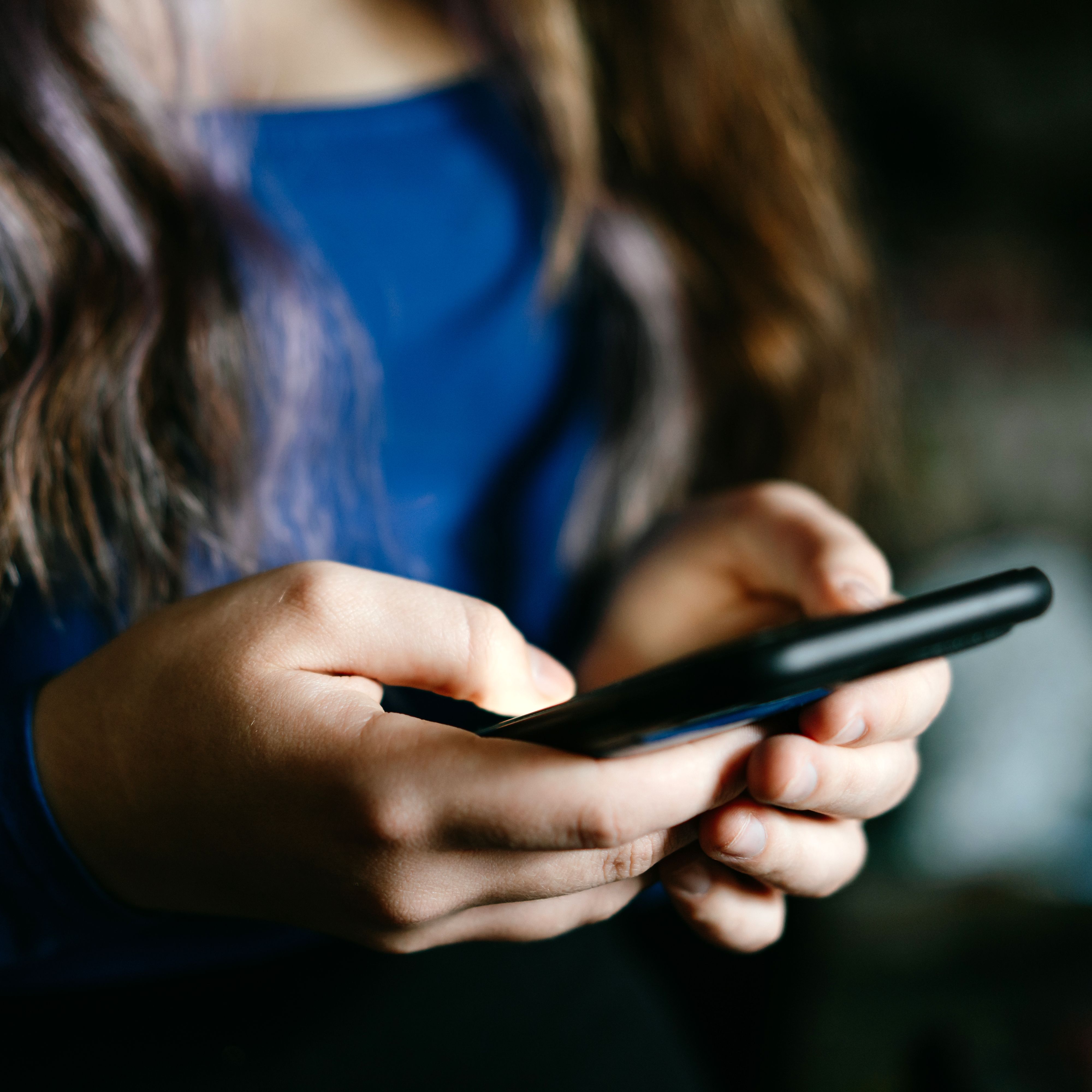 A focused view of individual's hands using a mobile phone indoors.