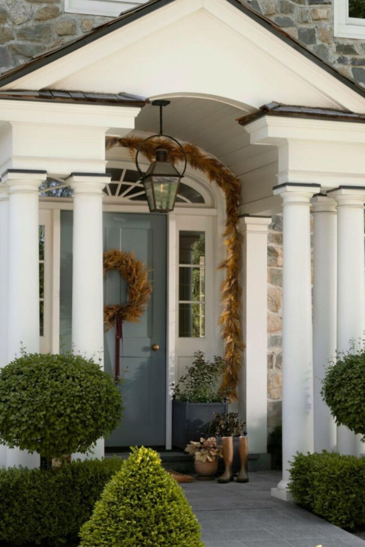 white pillared porch on a stone home decorated for thanksgiving with golden foliage garland and door wreath