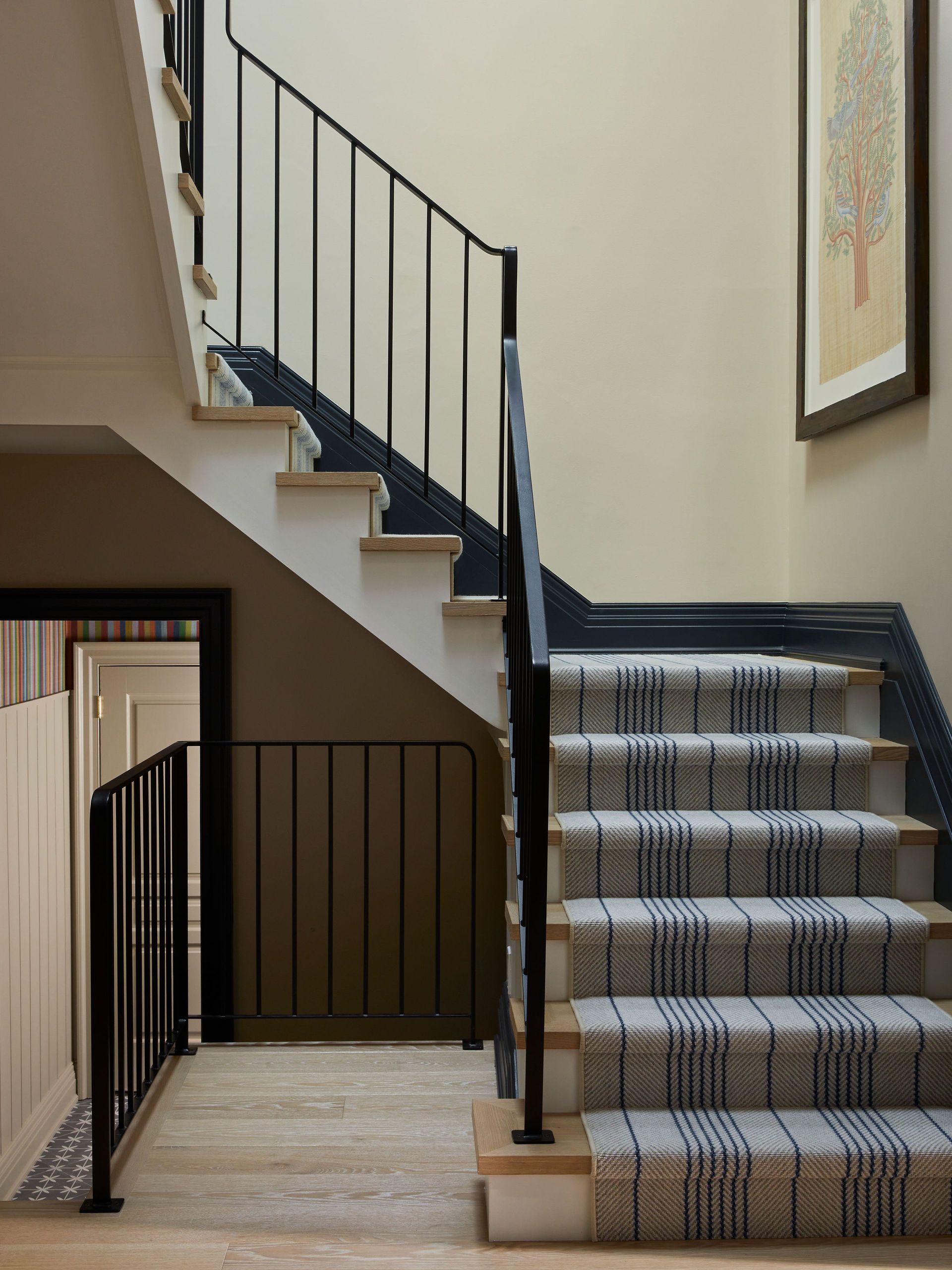 A modern staircase with a black metal railing and a striped runner leading up the treds.