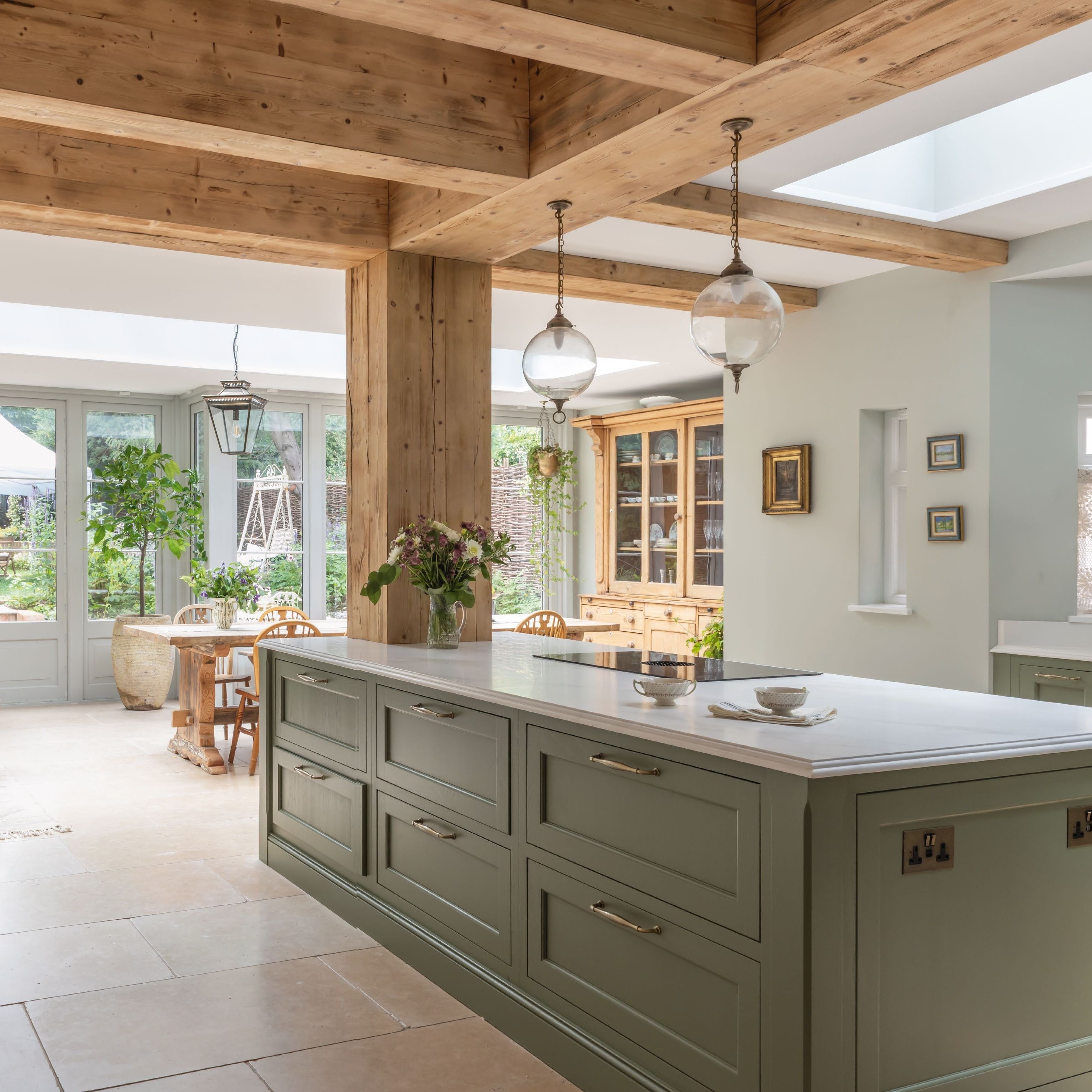 open plan kitchen diner with orangery style extension, wooden ceiling and supporting beams, green kitchen units and stone floor tiles