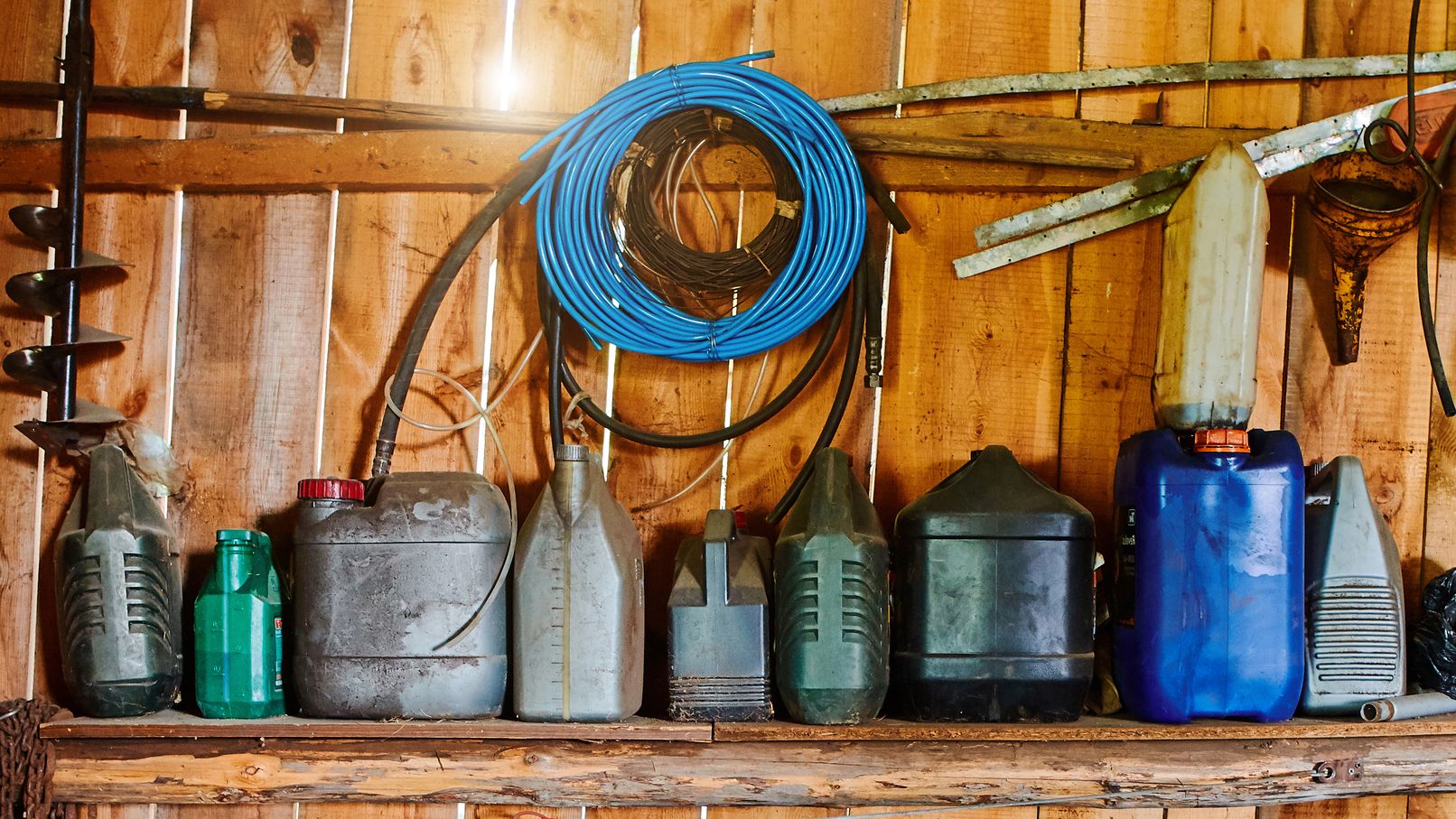 A group of old canisters and cylinders stand on shelves in a wooden shed