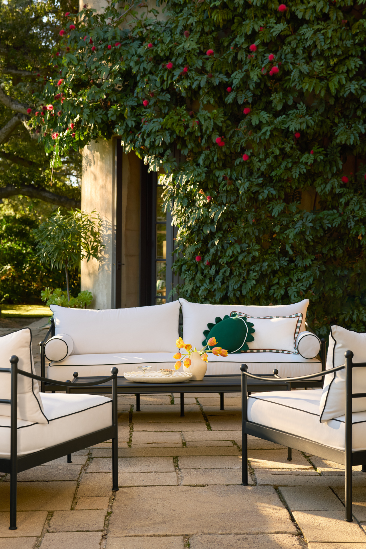an outdoor patio with a couch and two accent chairs with white cushions, a metal coffee table, and decorative pillows