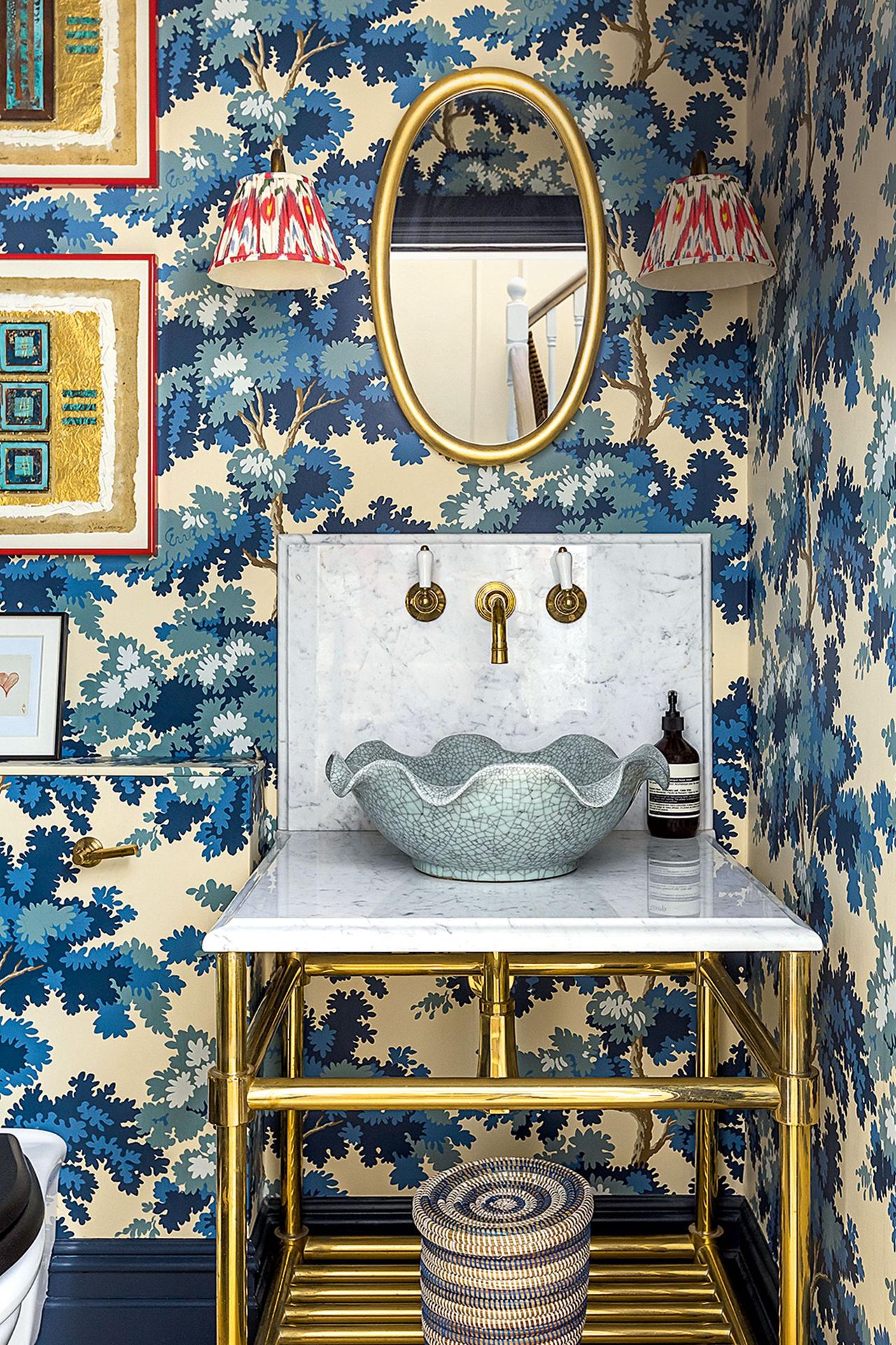 Bold blue floral wallpaper in bathroom with red wall lights and scalloped shape basin