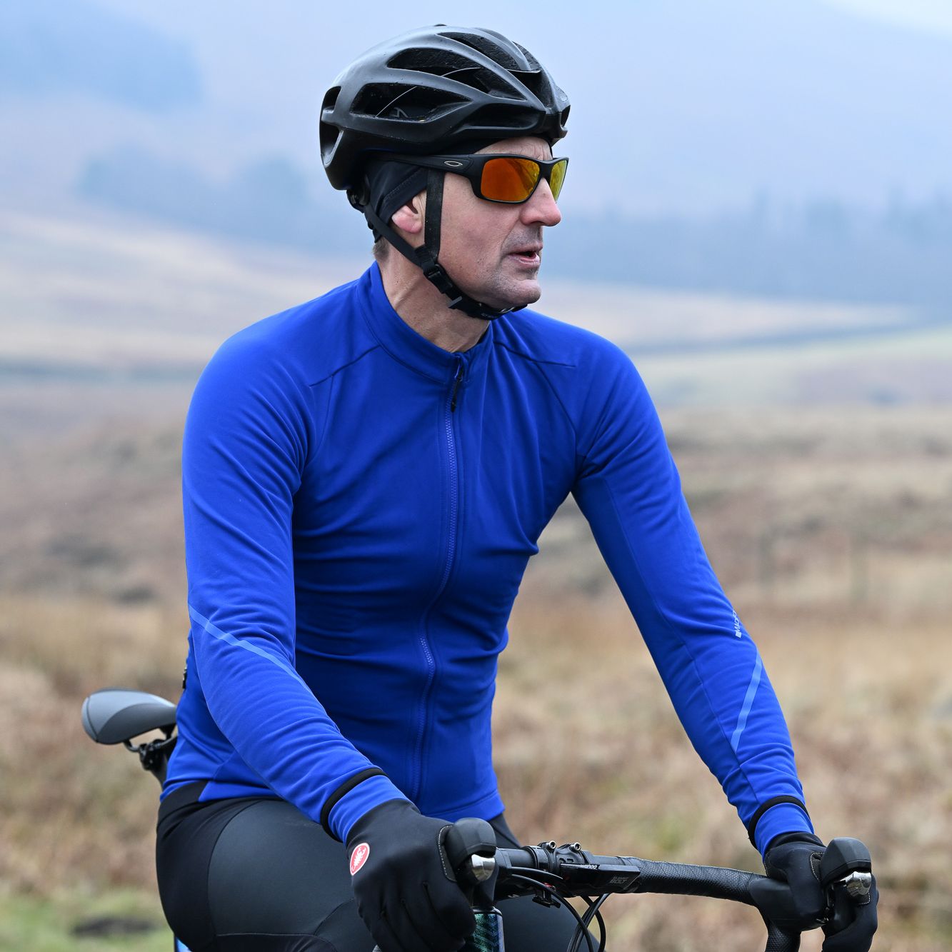 Man sitting on the top tube of a bike wearing a blue Madison DTE Isoler Thermal Long Sleeve Jacket