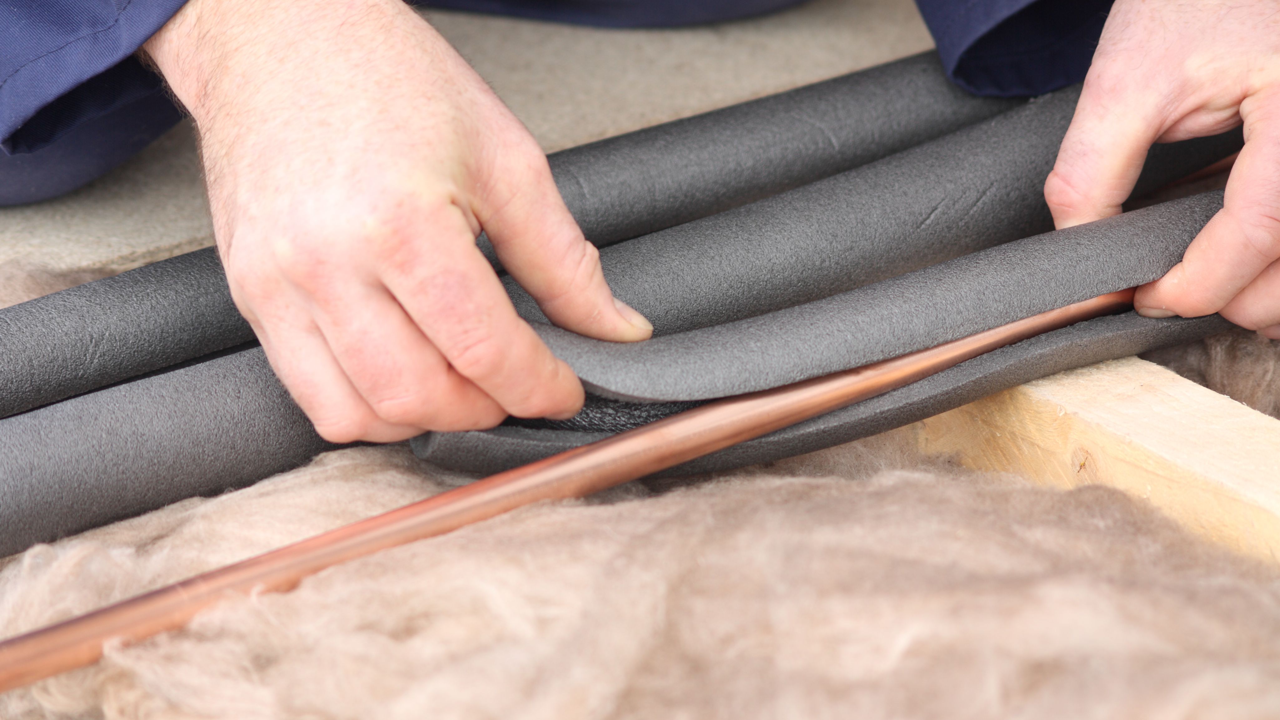 Hands hold an insulation wrap to cover pipes.