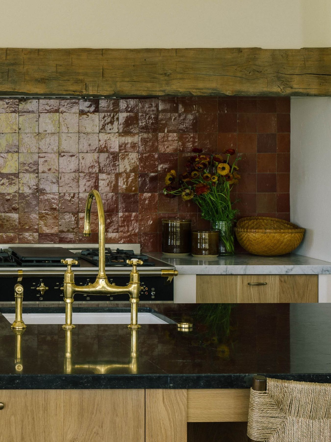 a contemporary meets rustic kitchen with oak cabinetry, rustic beams, and oxblood red zellige tile backsplash behind the range cooker