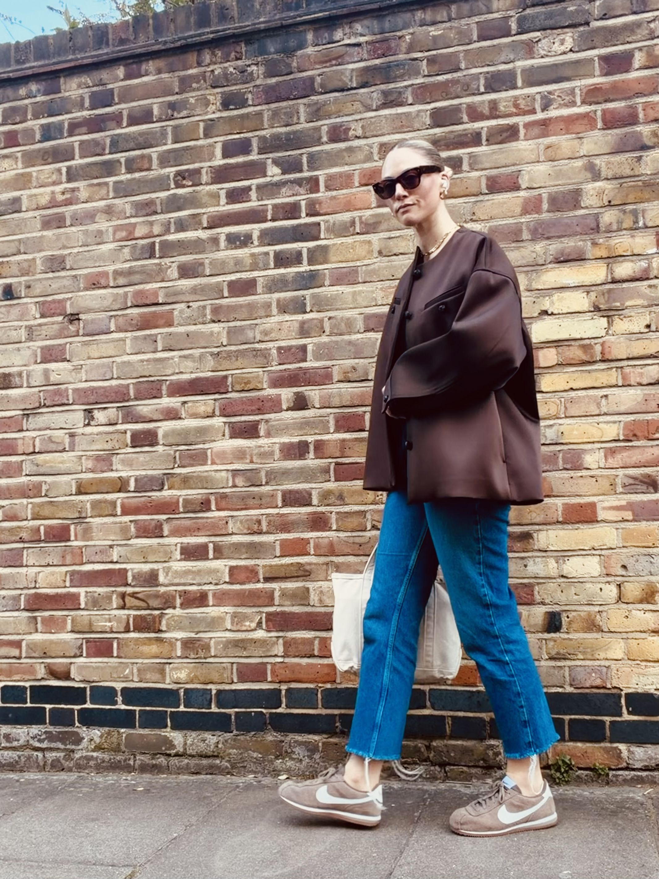 Brooke Ely Danielson styles Nike Cortez sneakers in taupe with ankle-length jeans and an oversize brown jacket