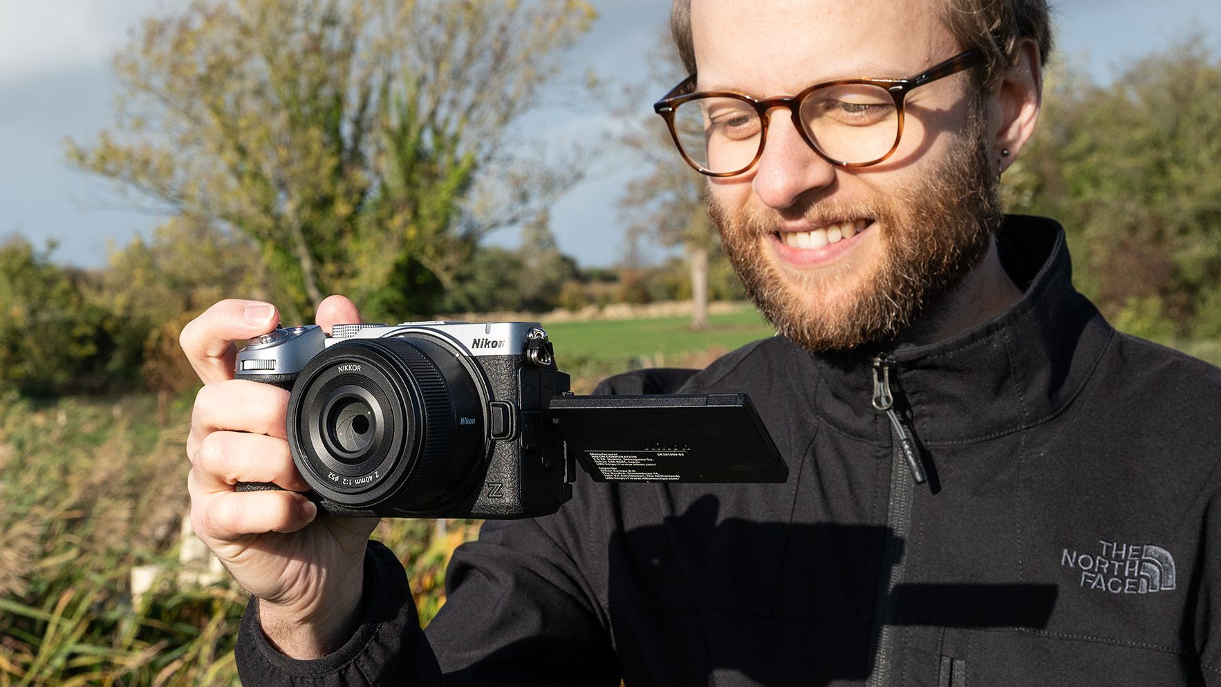 Mike Harris wearing a black jacket holding the Nikon Z5IIC on a green background