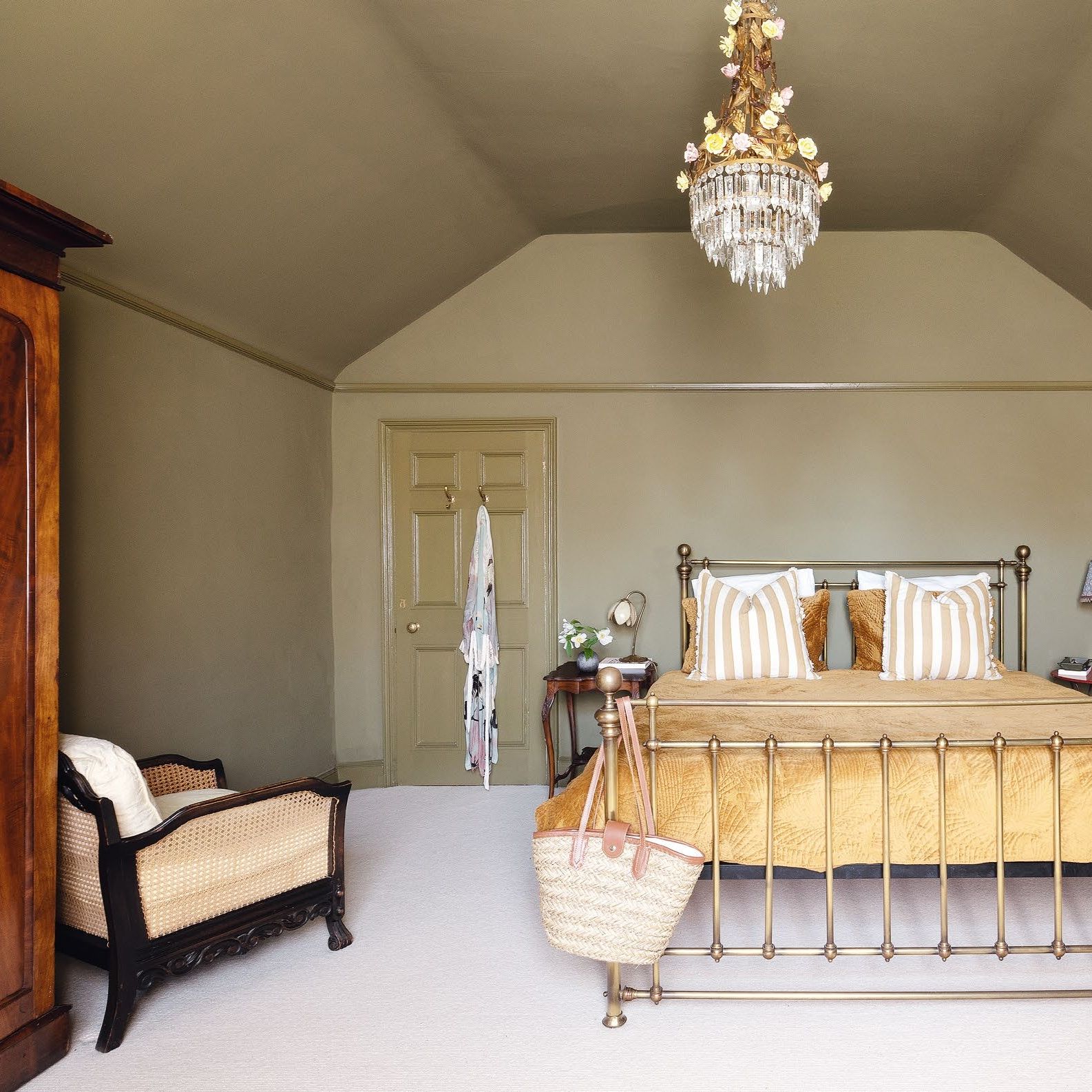 Bedroom colour drenched in earthy green, with chandelier and metal framed bed