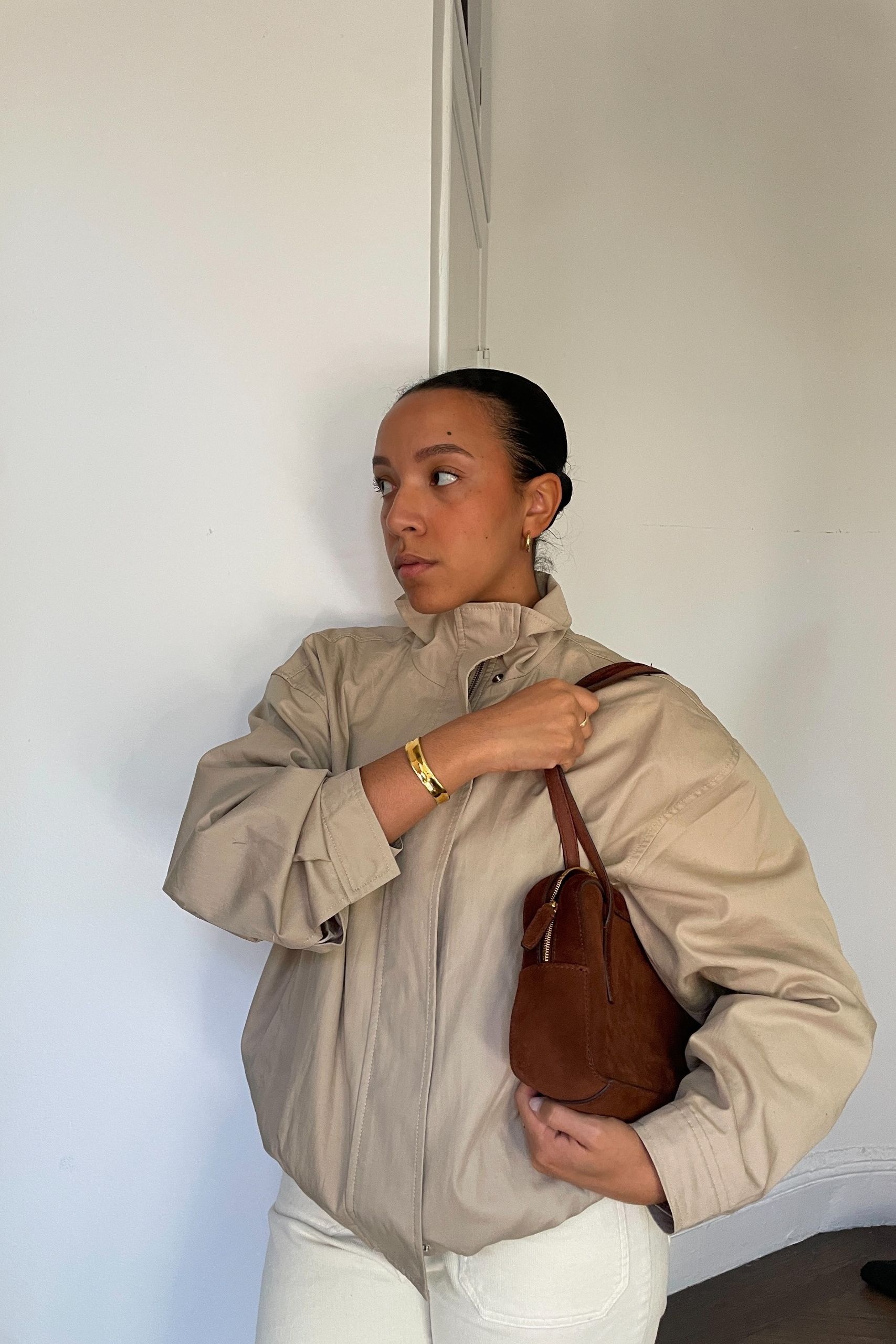 Lauren Tappan wearing a funnel-neck jacket, white pants, and a brown bag